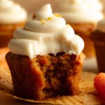 side view of a vegan carrot cake cupcake with a bite taken out of it.
