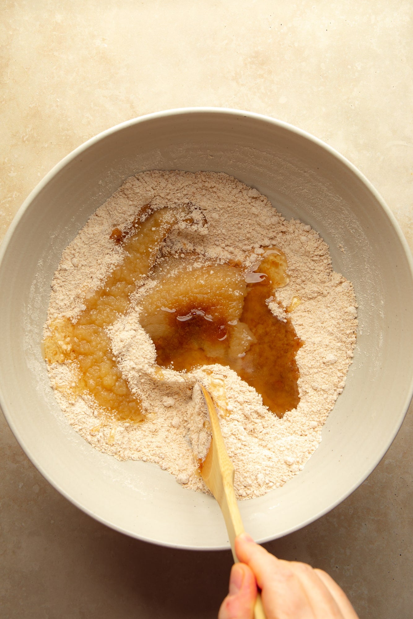 overhead view of a hand using a wooden spoon to stir the ingredients for vegan carrot cake cupcakes together in a bowl.