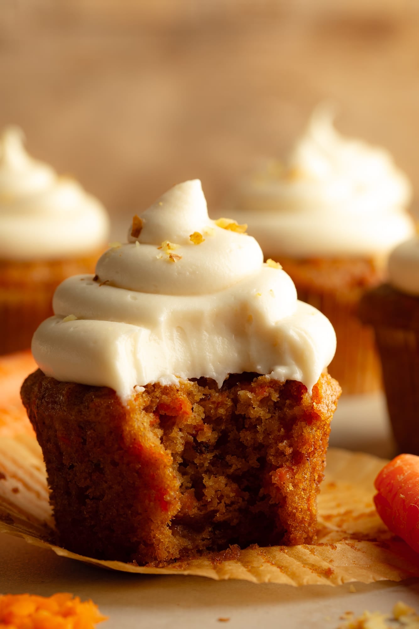 side view of a vegan carrot cake cupcake with a bite taken out of it.