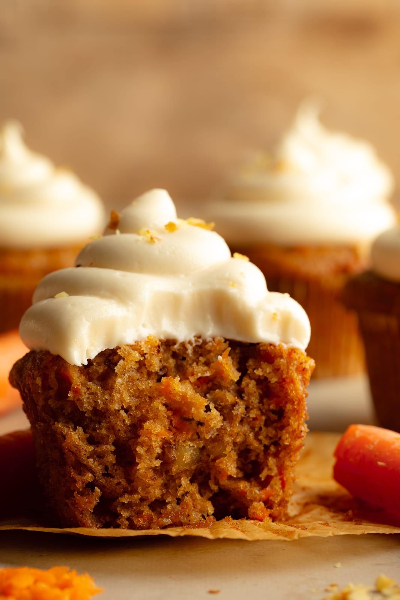 side view of a vegan carrot cake cupcake with a bite taken out of it.