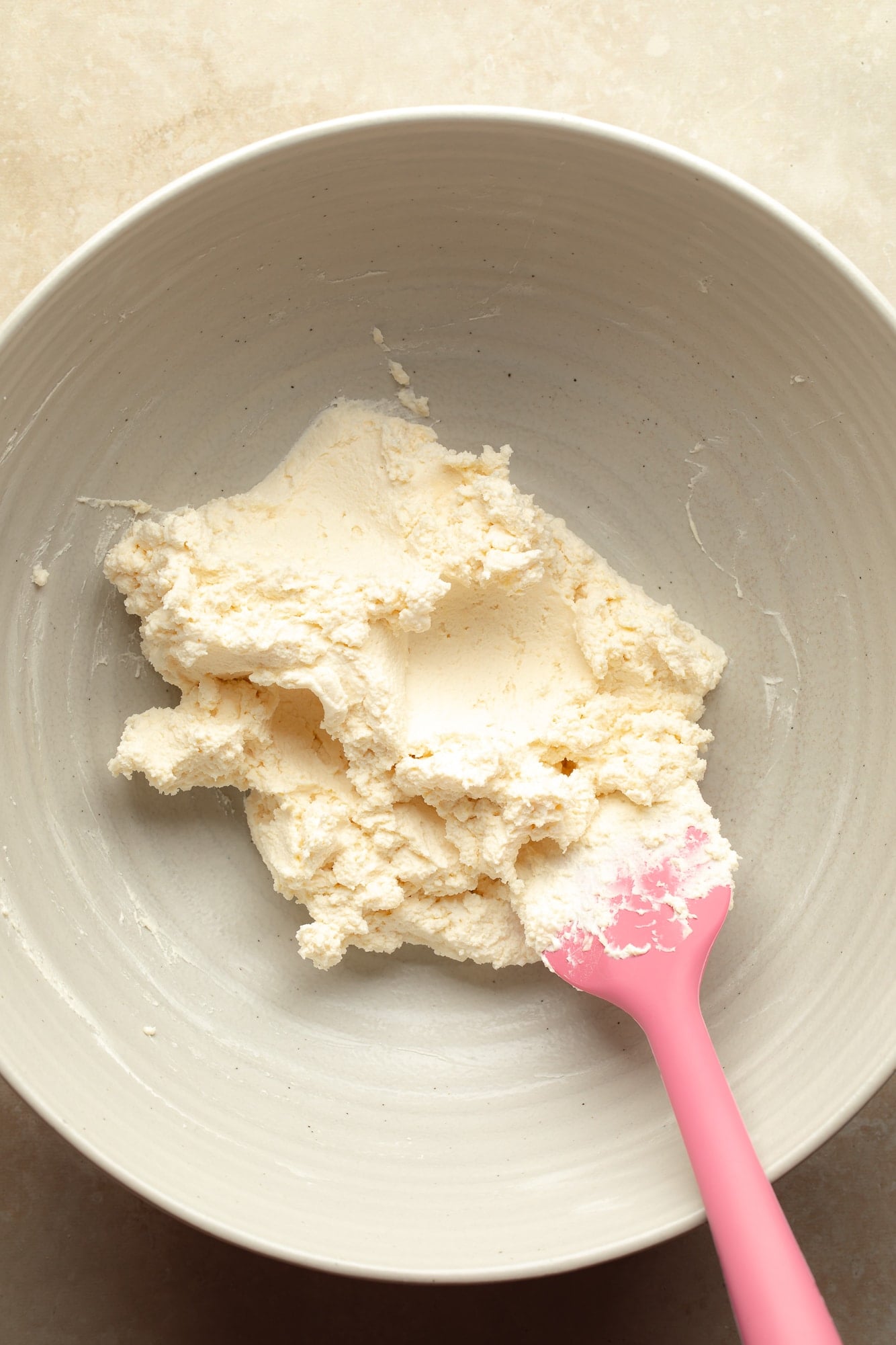 overhead view of a pink spatula stirring whipped vegan butter and vegan cream cheese for Vegan Cream Cheese Frosting in a large bowl.