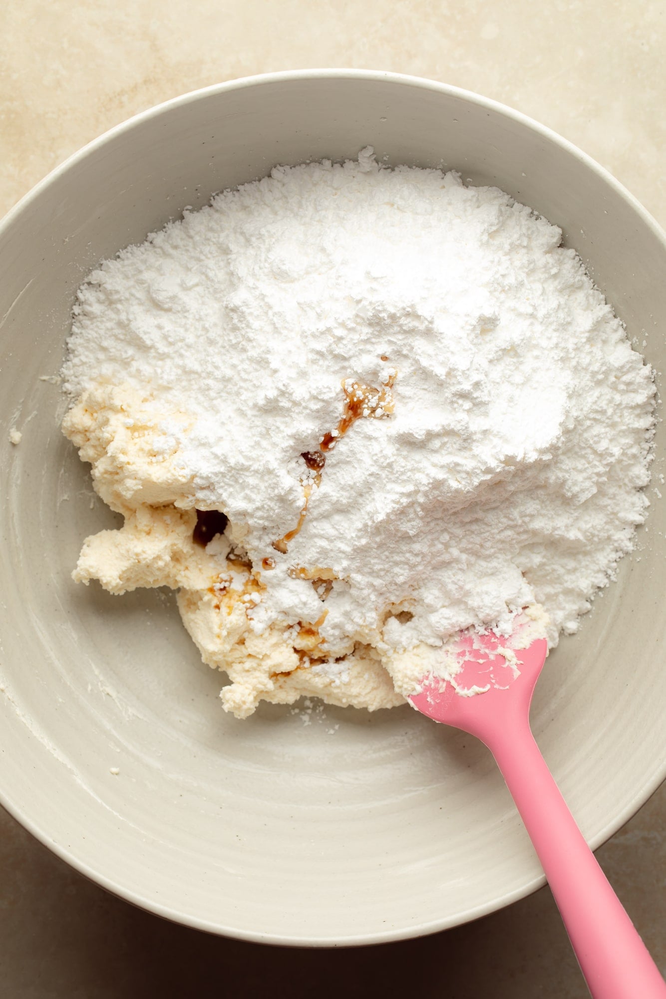 the ingredients for vegan cream cheese frosting together in a large bowl with a pink spatula.