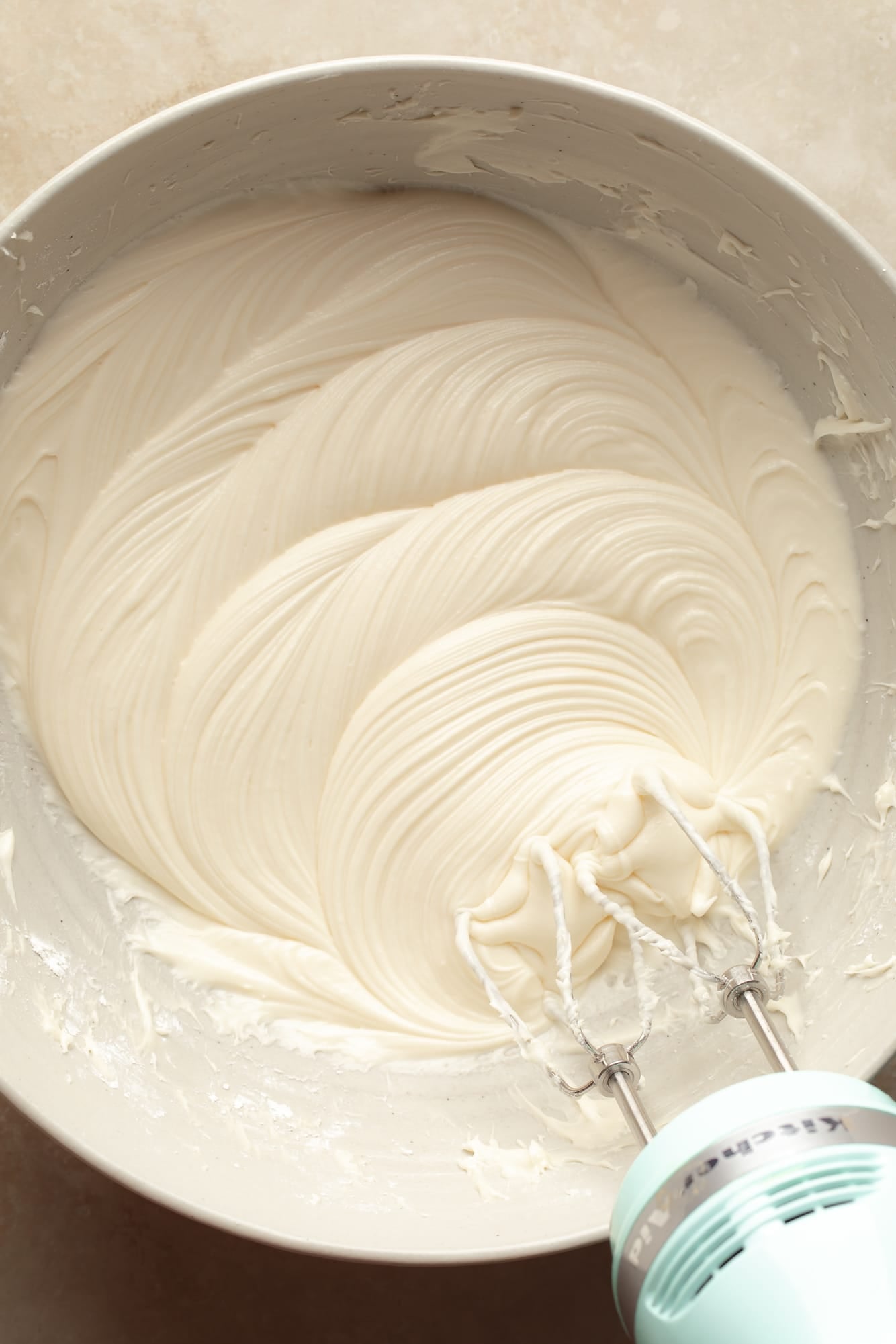 overhead view of an electric mixer beating vegan cream cheese frosting in a bowl.