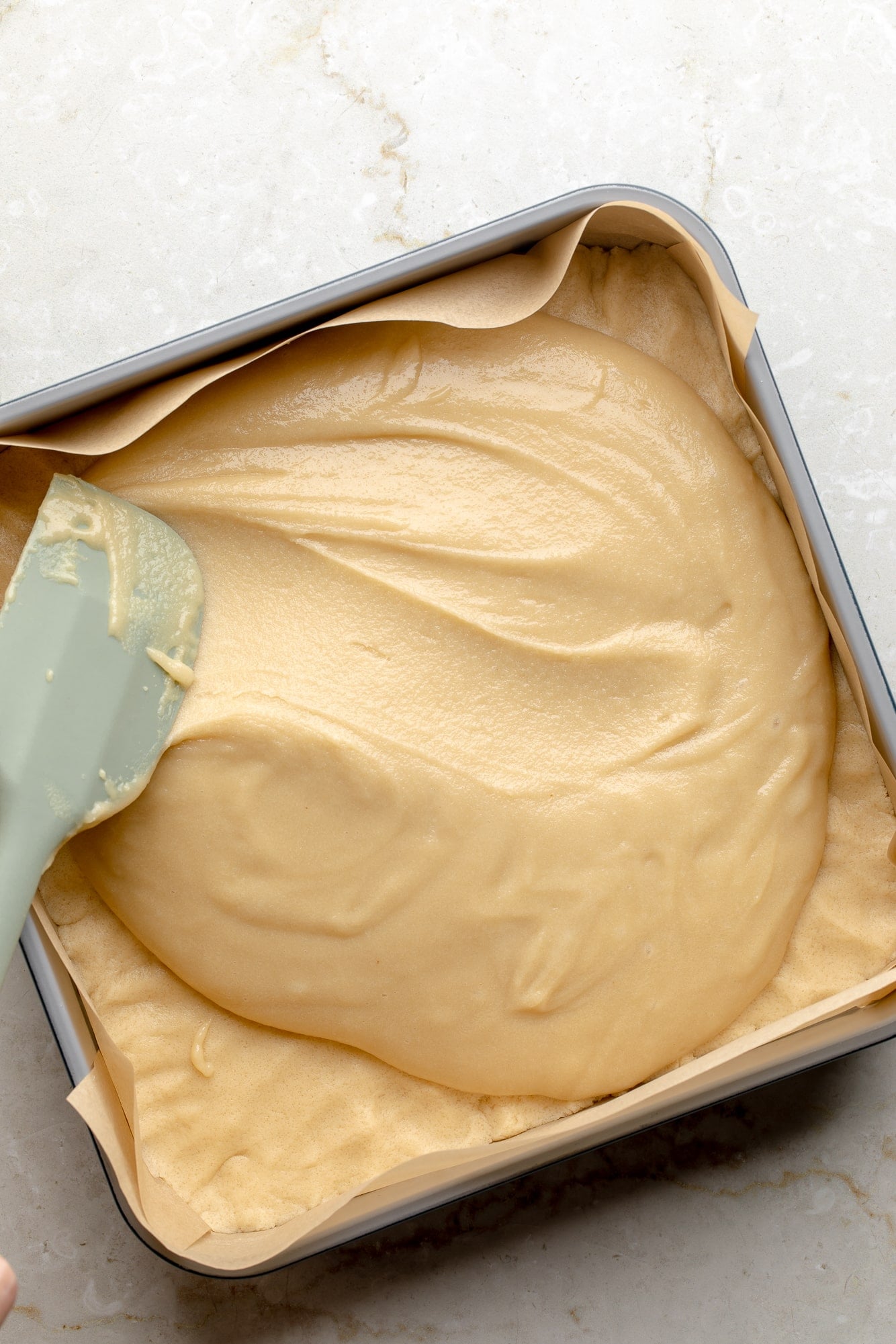 overhead view of a spatula spreading almond frangipane onto a cookie crust in a baking pan.