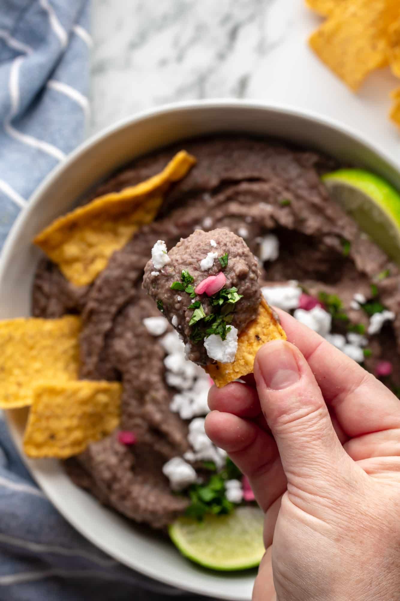 close up on a hand holding a tortilla chip topped with a scoop of black bean dip.