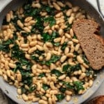 overhead view of a slice of bread in a skillet full of braised white beans and kale.