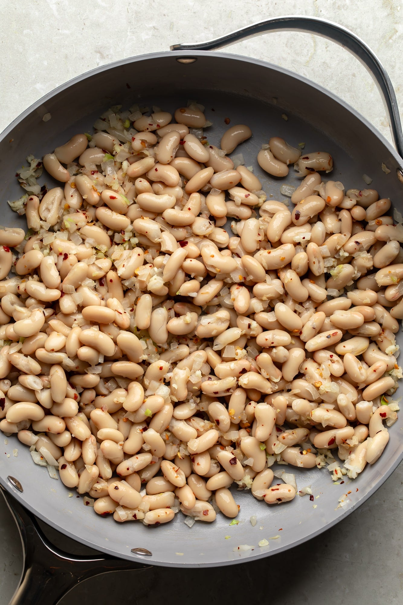 overhead view of braised white beans in a skillet.