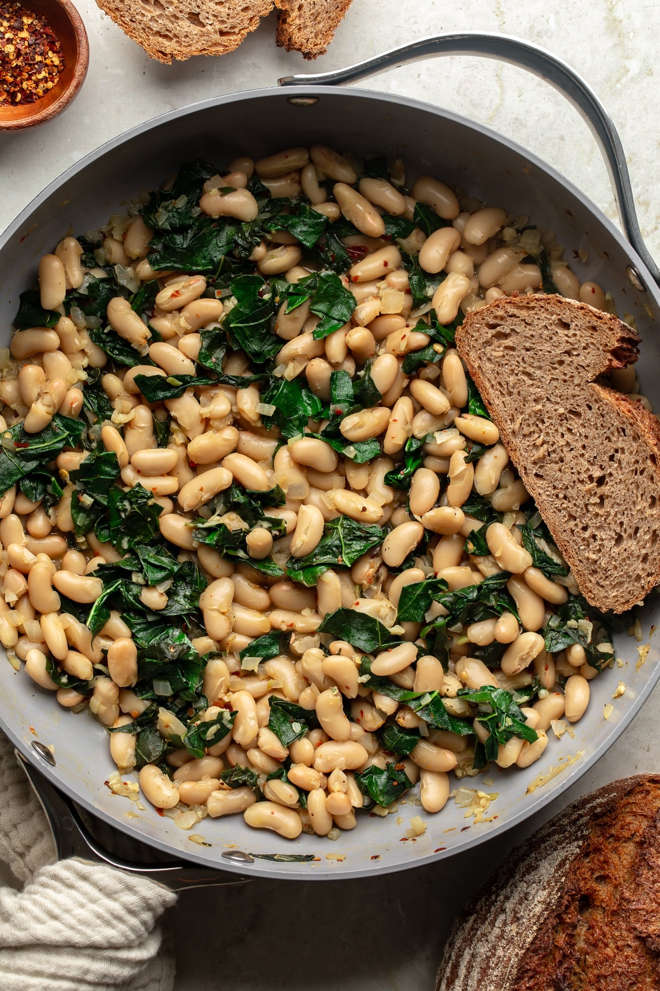 overhead view of a slice of bread in a skillet full of braised white beans and kale.