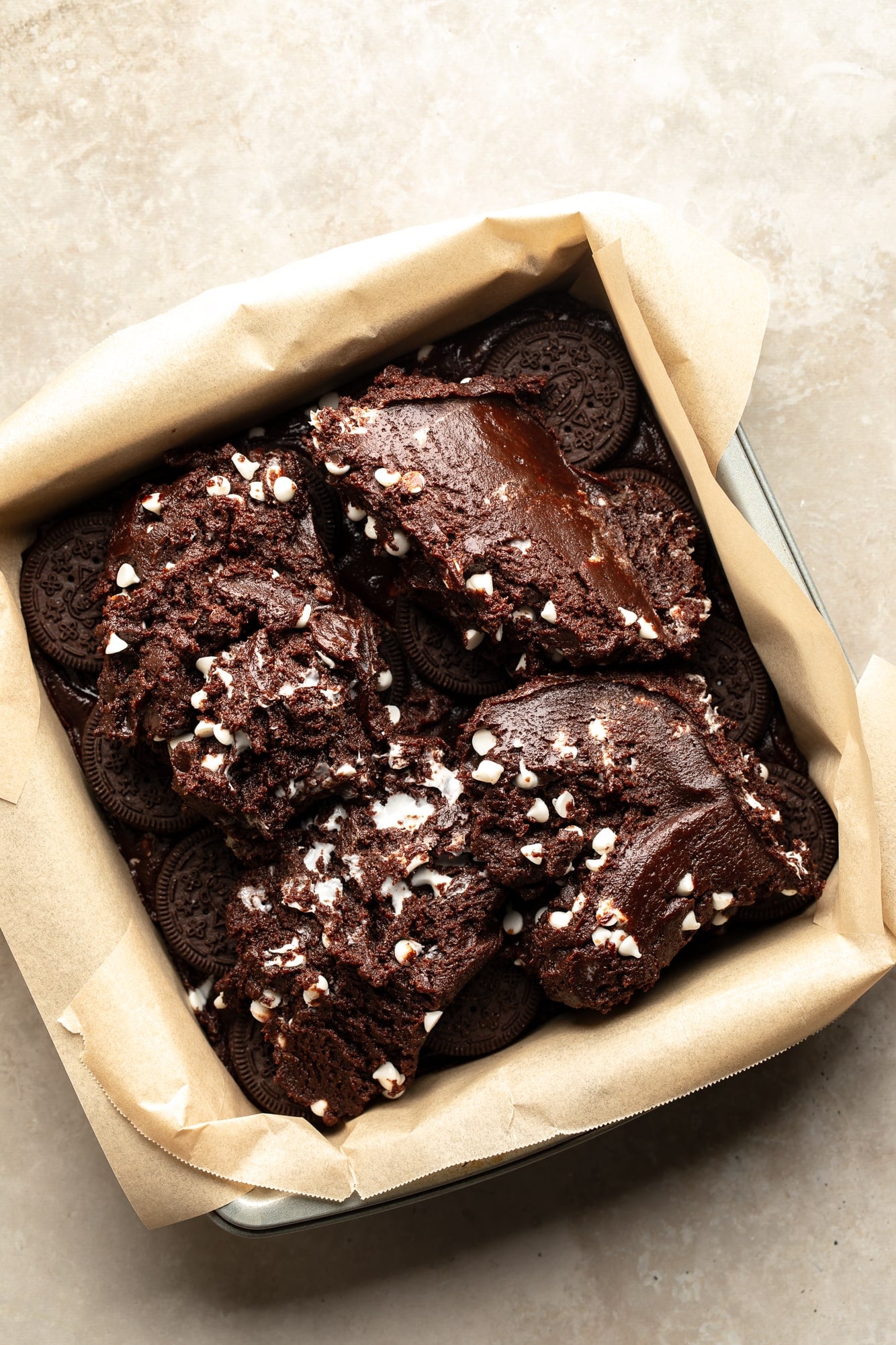 overhead view of vegan brownie batter being layered on top of Oreo cookies in a baking pan.