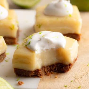 Side view of a vegan key lime pie bar topped with vegan whipped cream with a bite taken out of it.
