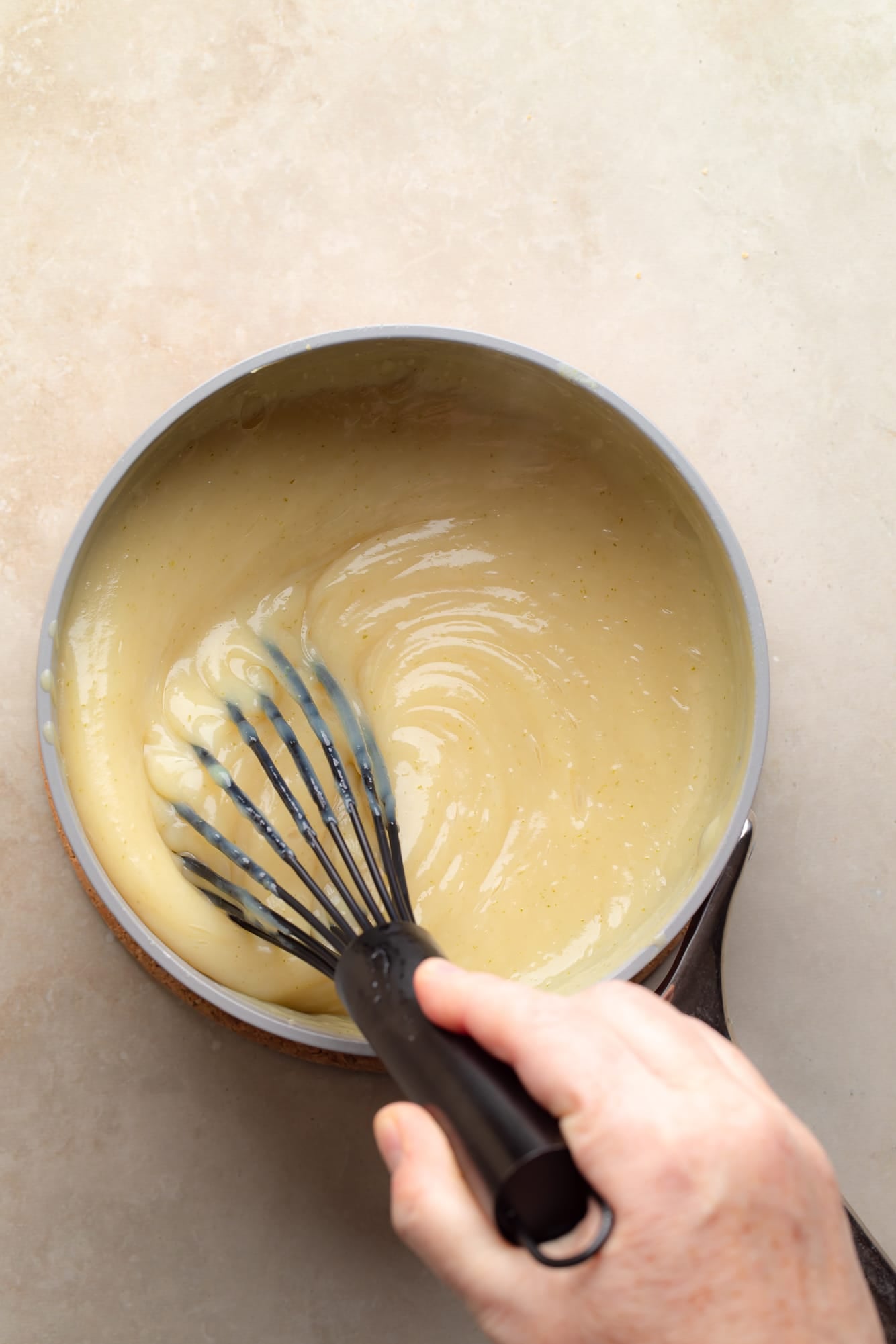 Overhead view of a hand using a black whisk to whisk liquid key lime pie filling in a sauce pan.
