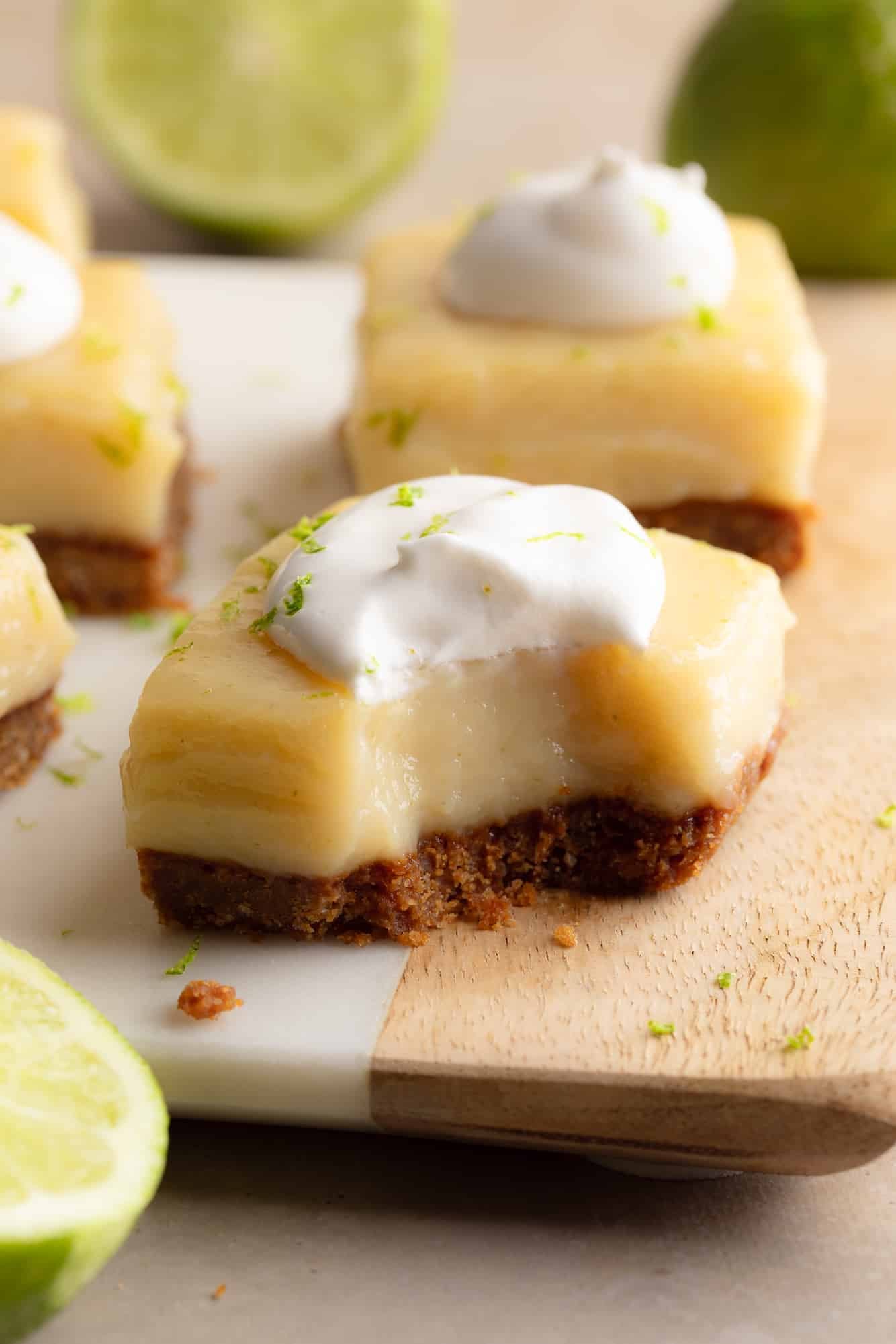 Side view of a vegan key lime pie bar topped with vegan whipped cream with a bite taken out of it.
