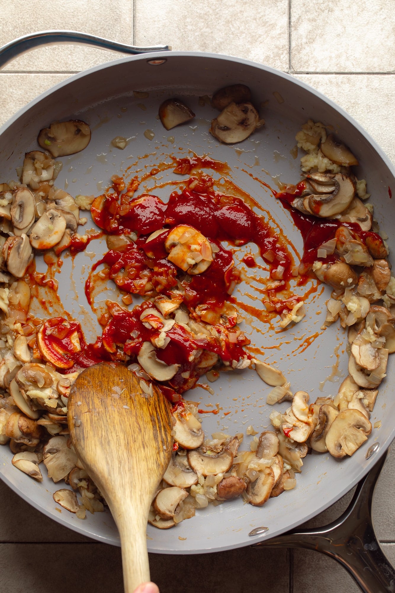 overhead view of a wooden spoon stirring mushrooms and gochujang in a skillet.