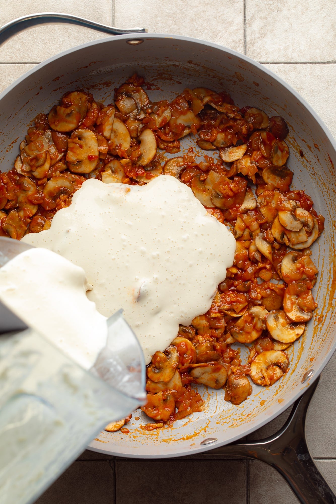 overhead view of cashew cream being poured into a skillet with gochujang-coated mushrooms.