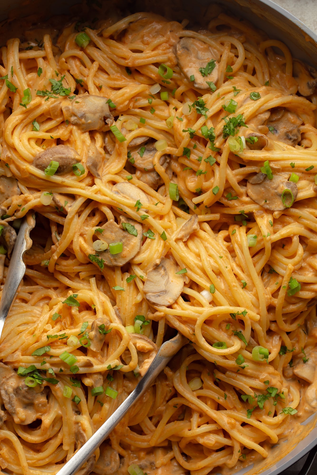 close up on metal tongs in a batch of creamy gochujang noodles.