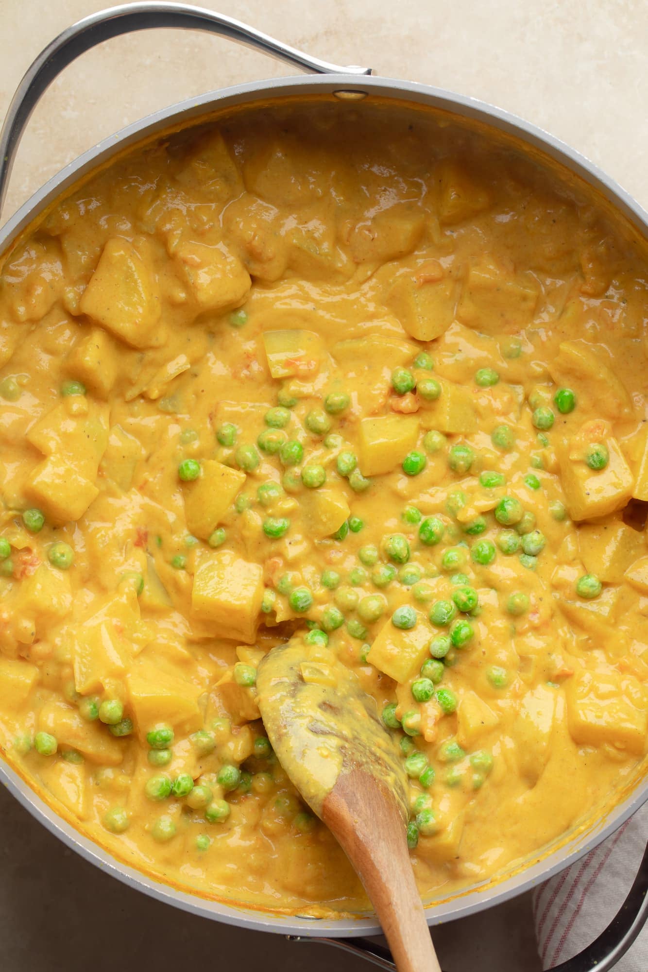overhead view of a wooden spoon stirring peas into a large pot of potato curry.