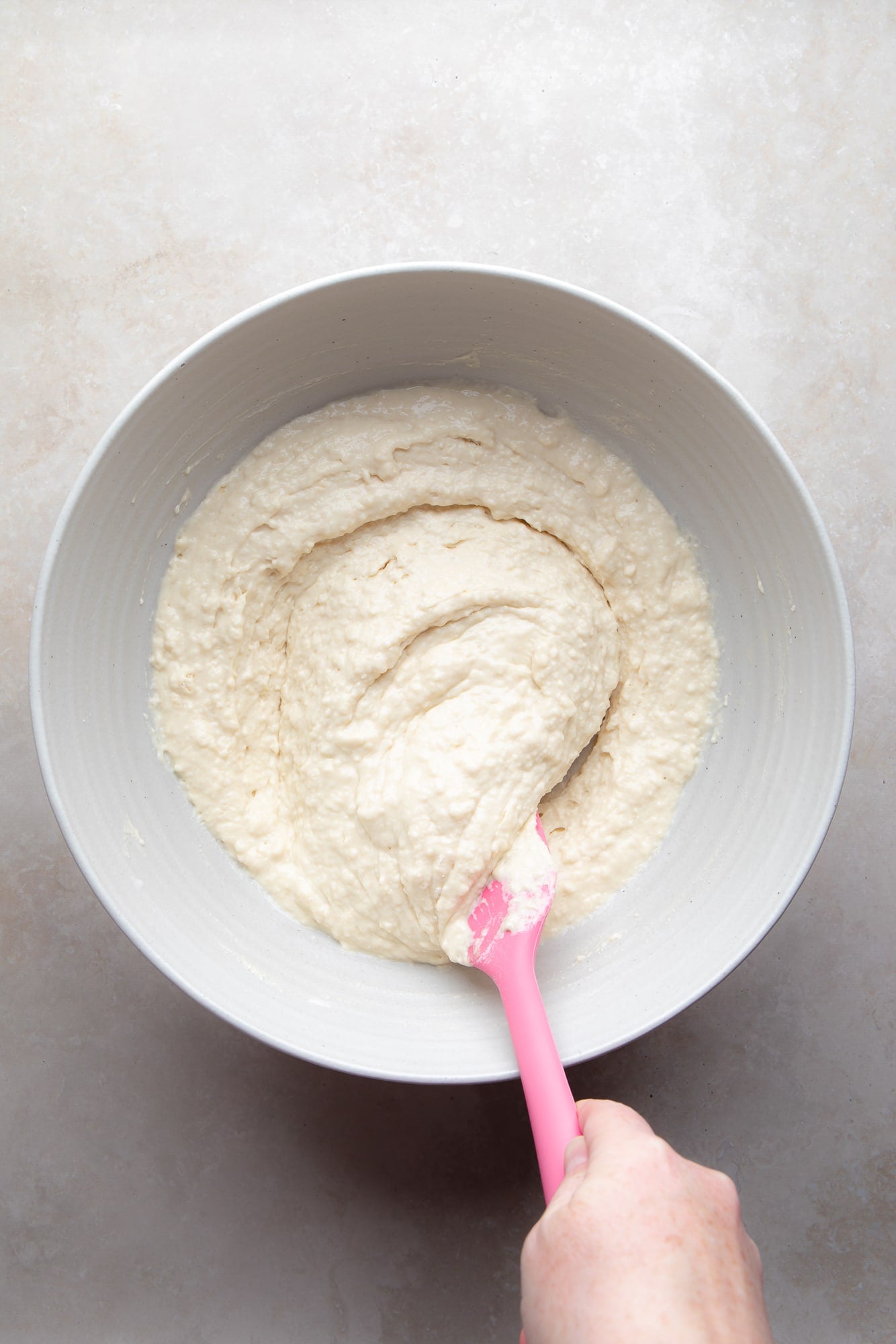 overhead view of a hand mixing vegan pancake batter with a pink spatula in a large bowl.