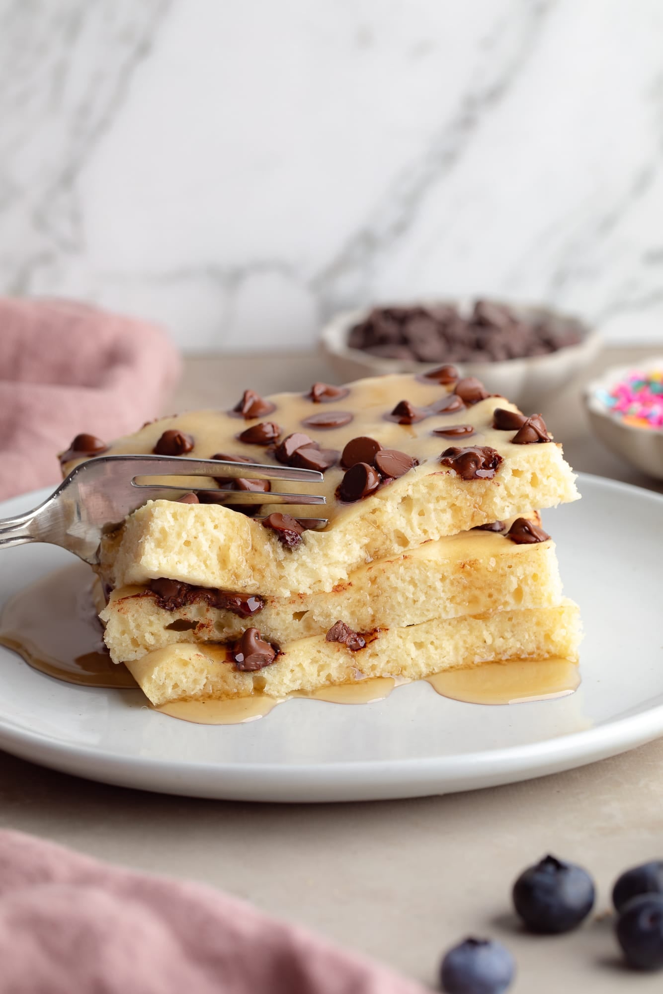 side view of a fork cutting into a stack of 3 sheet pan pancakes on a plate.