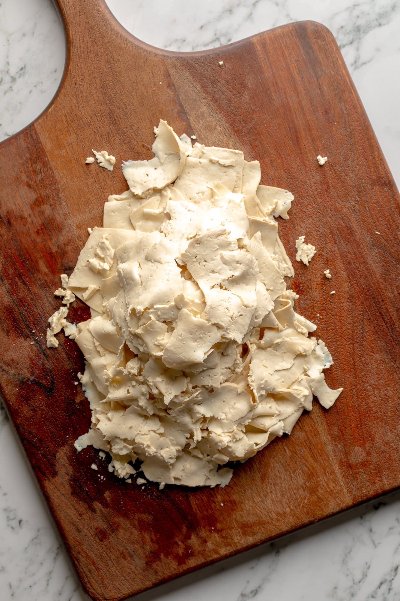 overhead view of a pile of thin tofu slices on a cutting board.