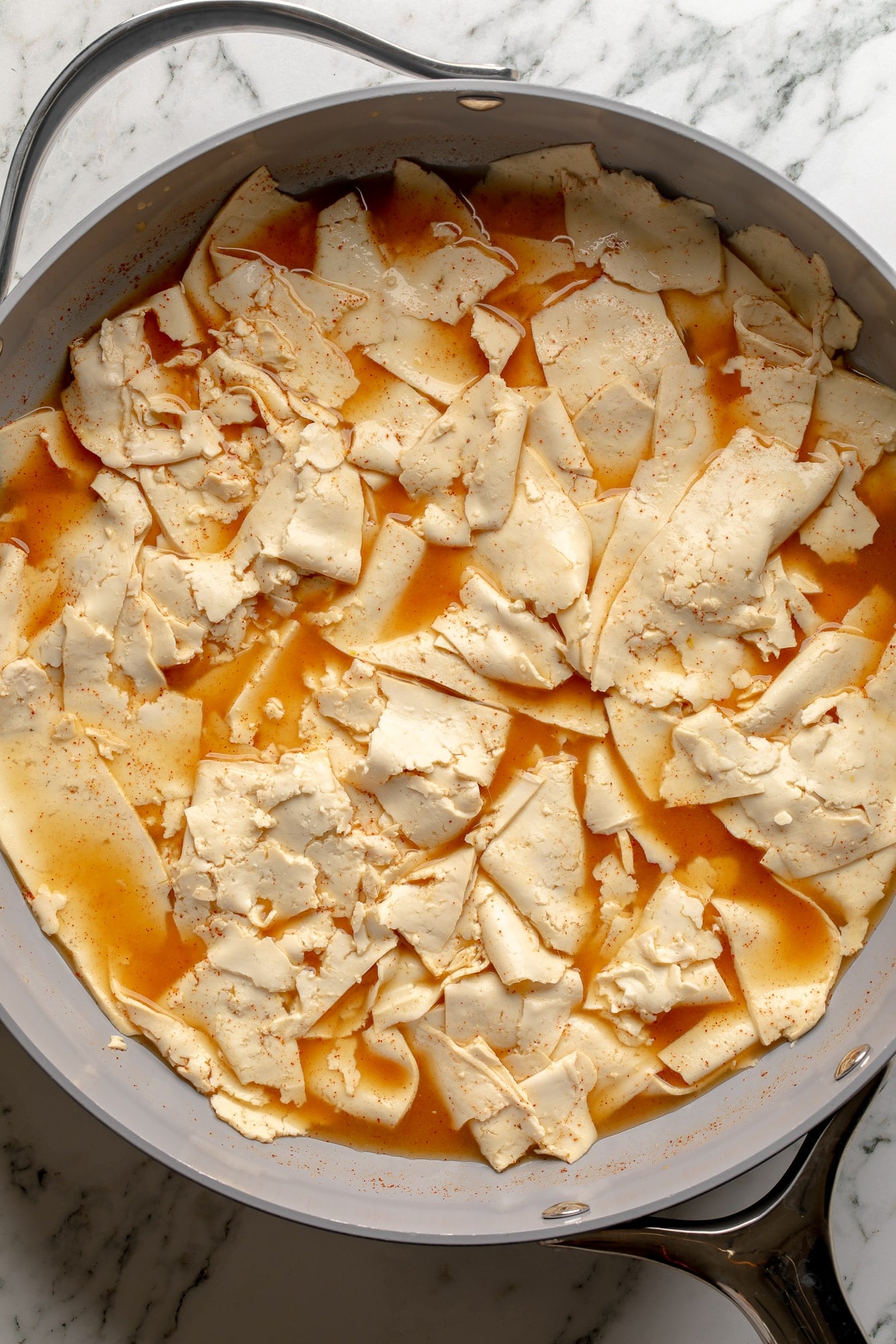 overhead view of thin tofu slices cooking in broth in a skillet.