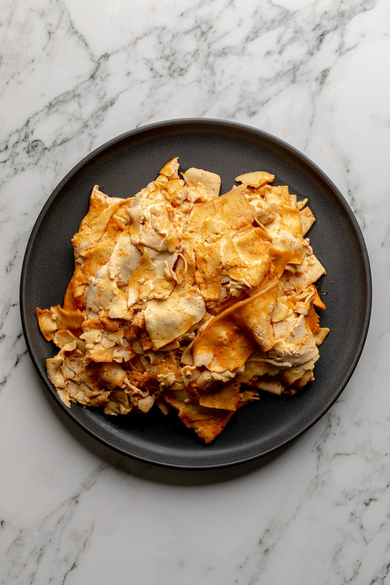 overhead view of a pile of cooked tofu lunch meat on a black plate.