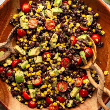 overhead view of a black bean salad with avocado, corn, and tomatoes in a large bamboo bowl.