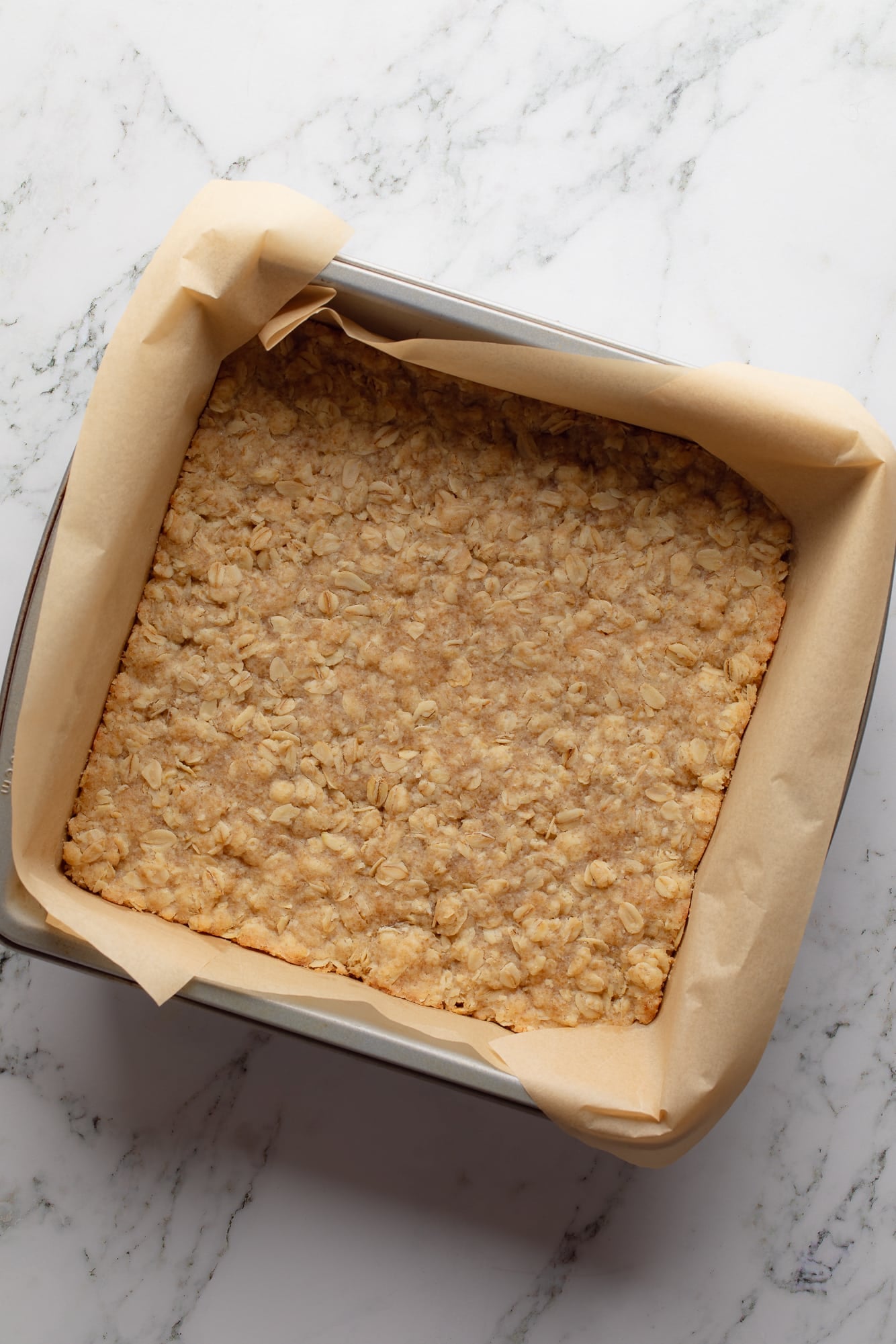 overhead view of the baked oatmeal crust for Chocolate Peanut Butter Oatmeal Bars in a baking pan.