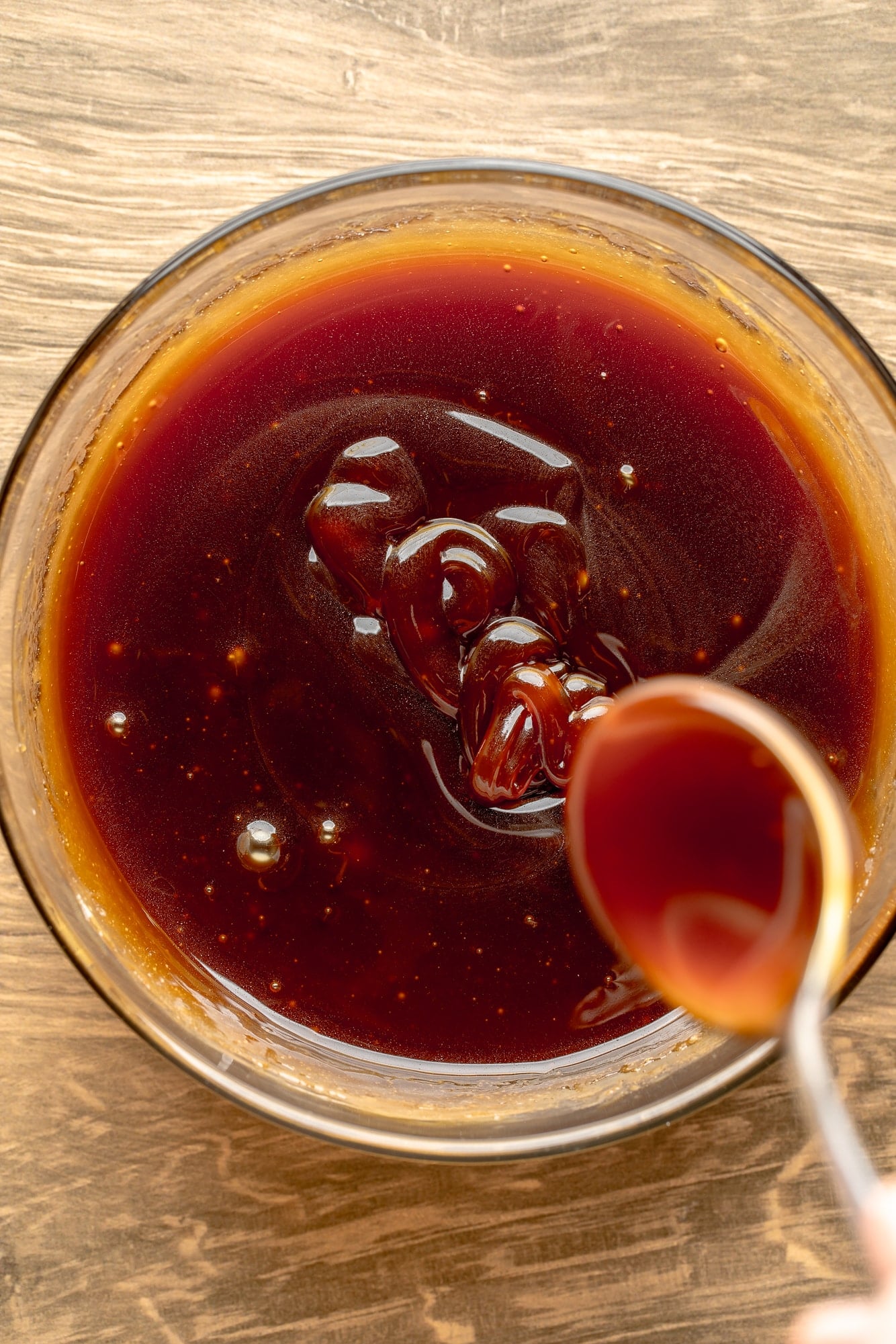 overhead view of a spoon held above a bowl of vegan salted caramel sauce.
