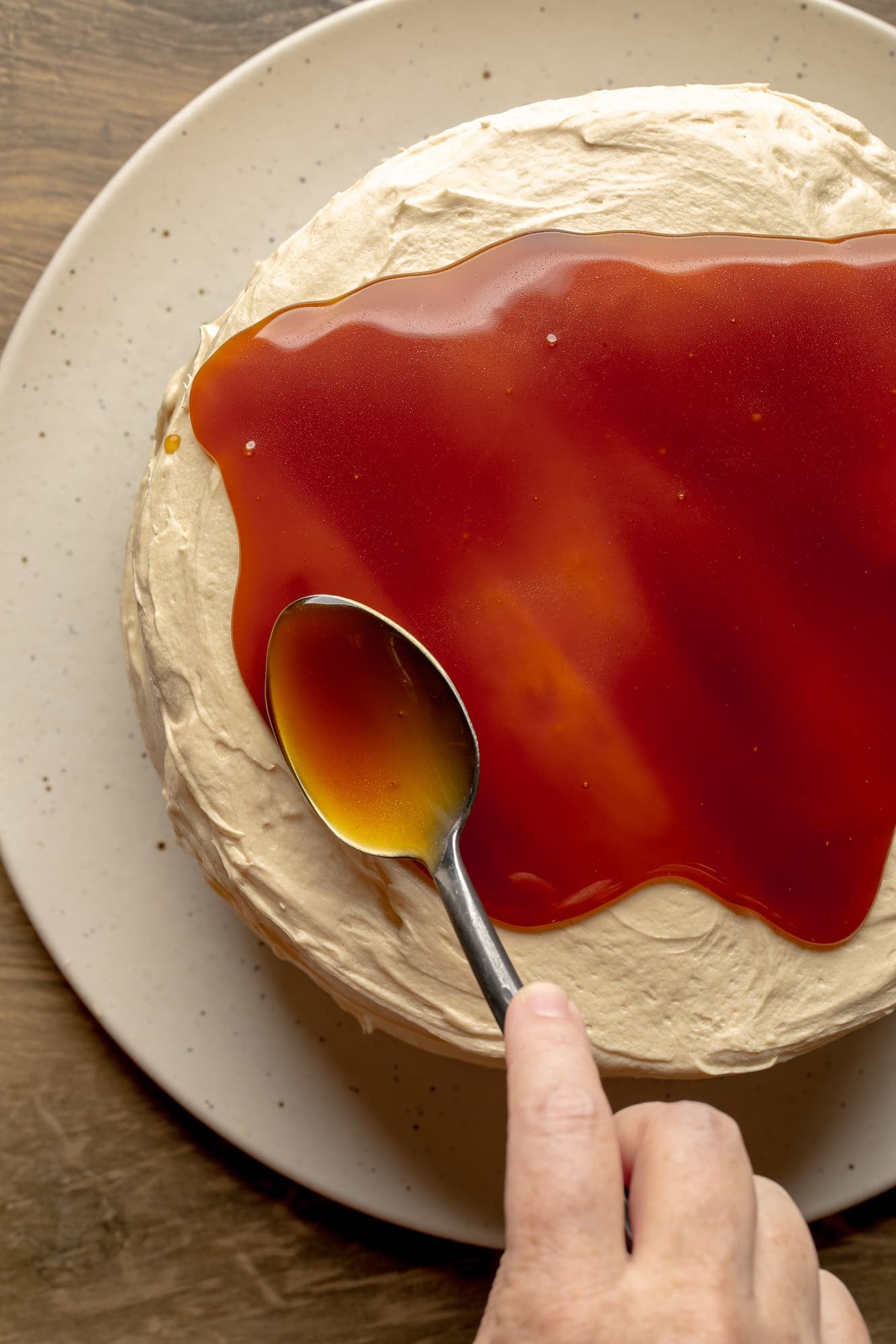 overhead view of a spoon spreading vegan salted caramel sauce on top of a vegan salted caramel chocolate cake.