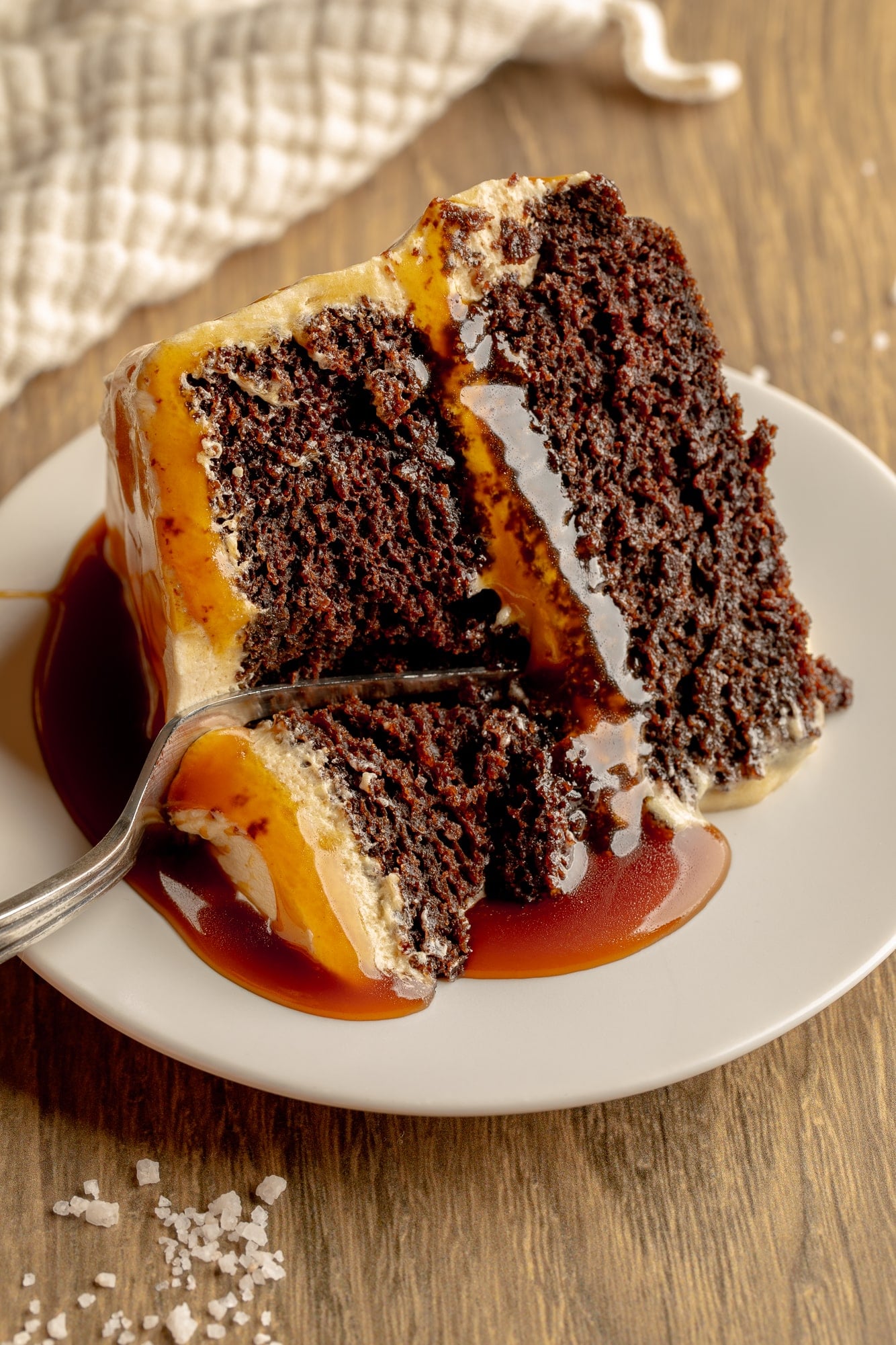side view of a fork cutting into a slice of vegan salted caramel chocolate cake.
