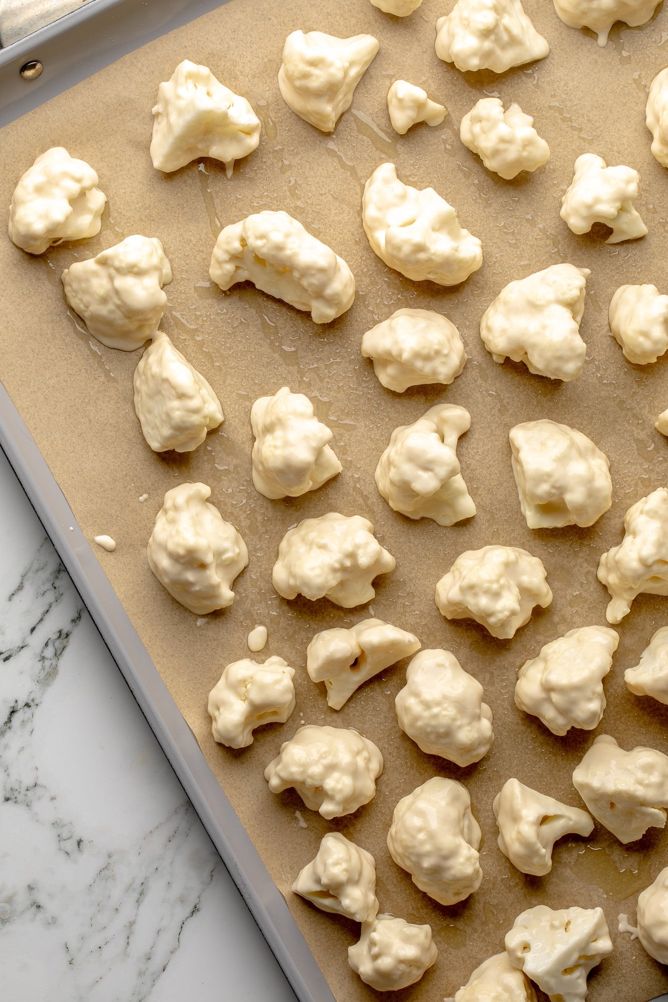overhead view of battered cauliflower florets on a baking sheet.