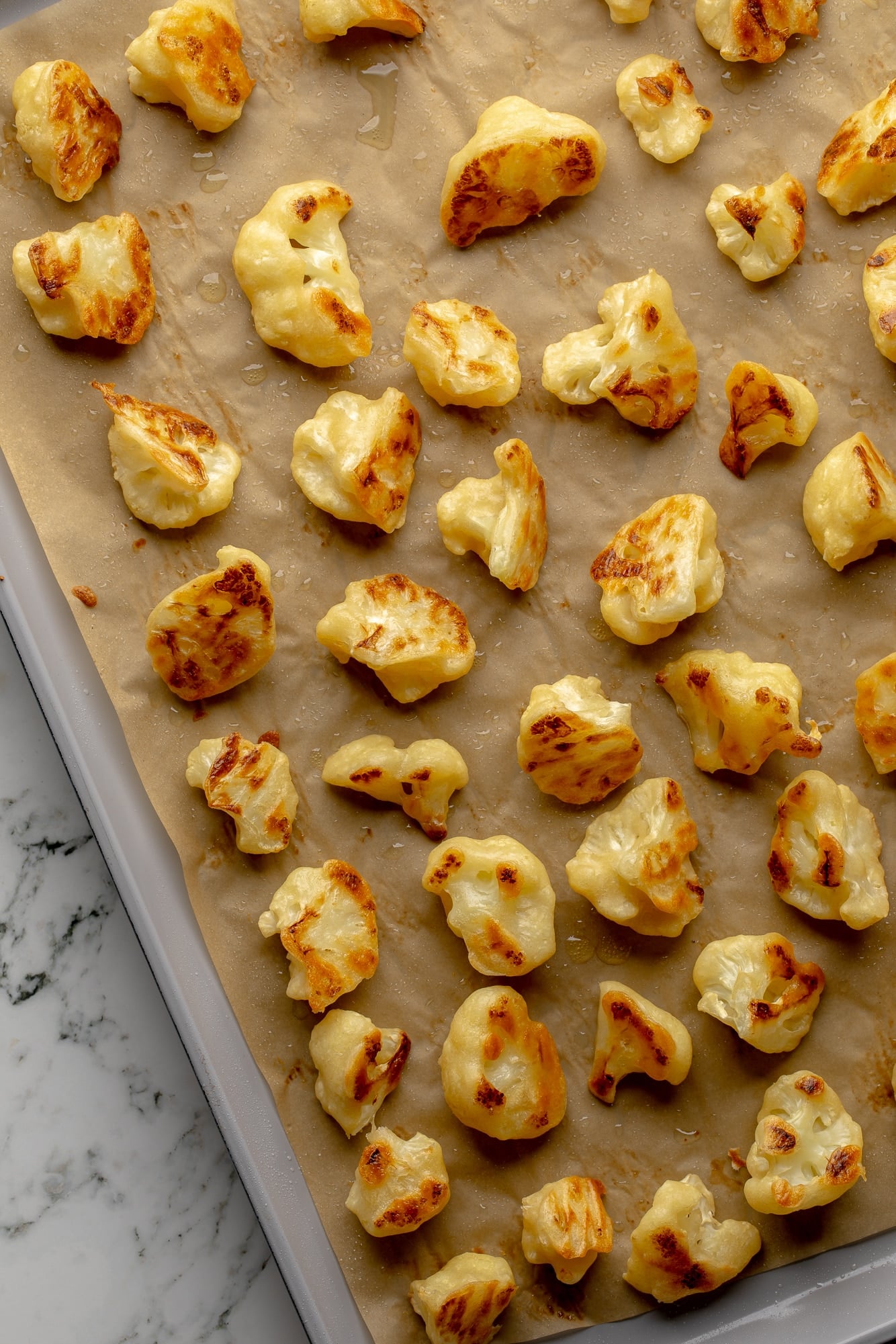 overhead view of battered and baked cauliflower florets on a baking sheet.