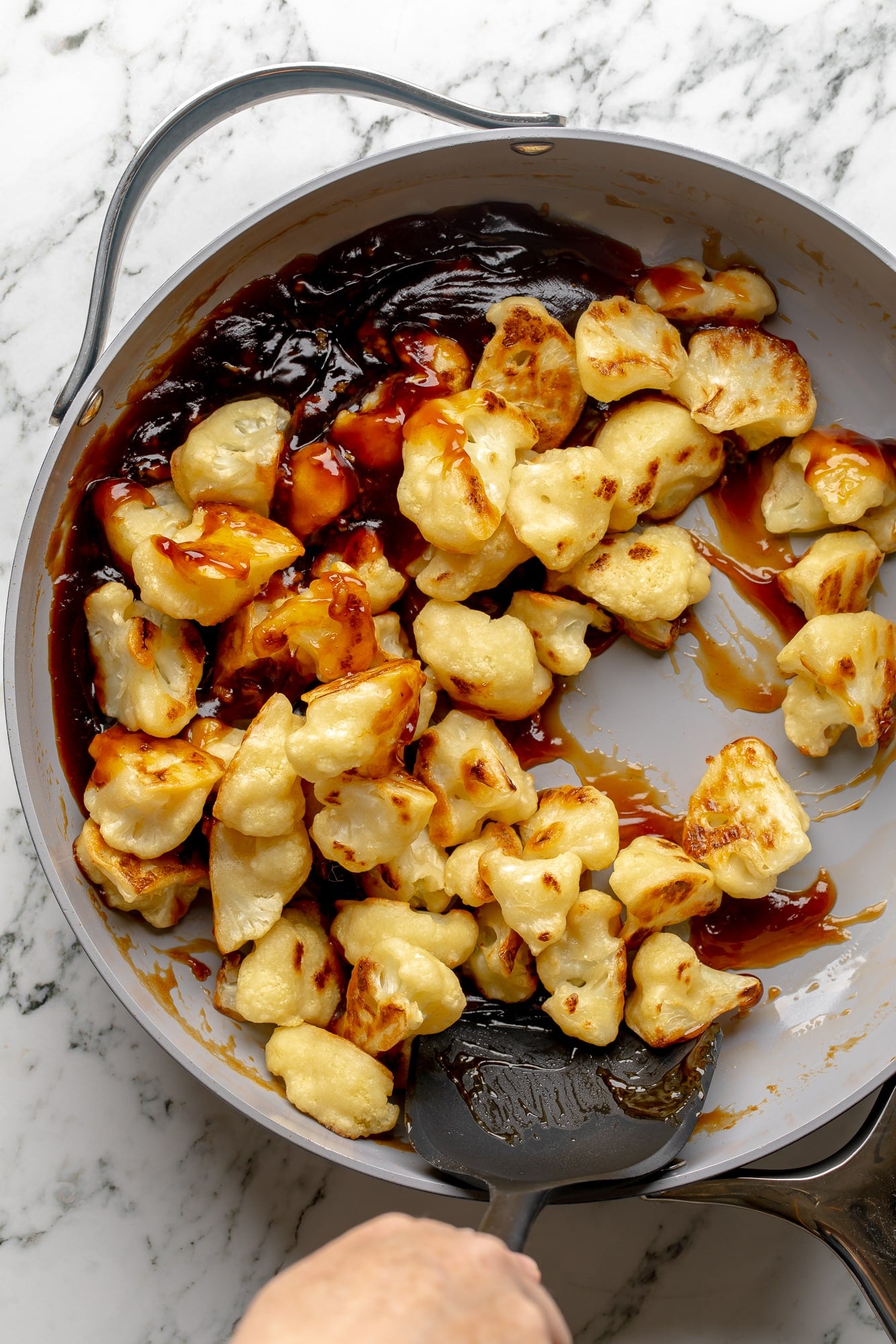 overhead view of baked cauliflower being tossed in sesame sauce in a skillet.
