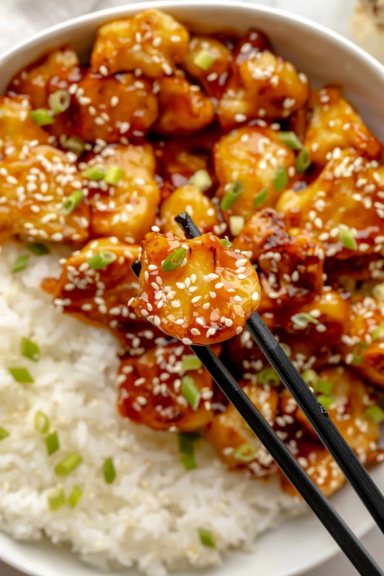 close up on chopsticks holding a piece of sesame cauliflower.