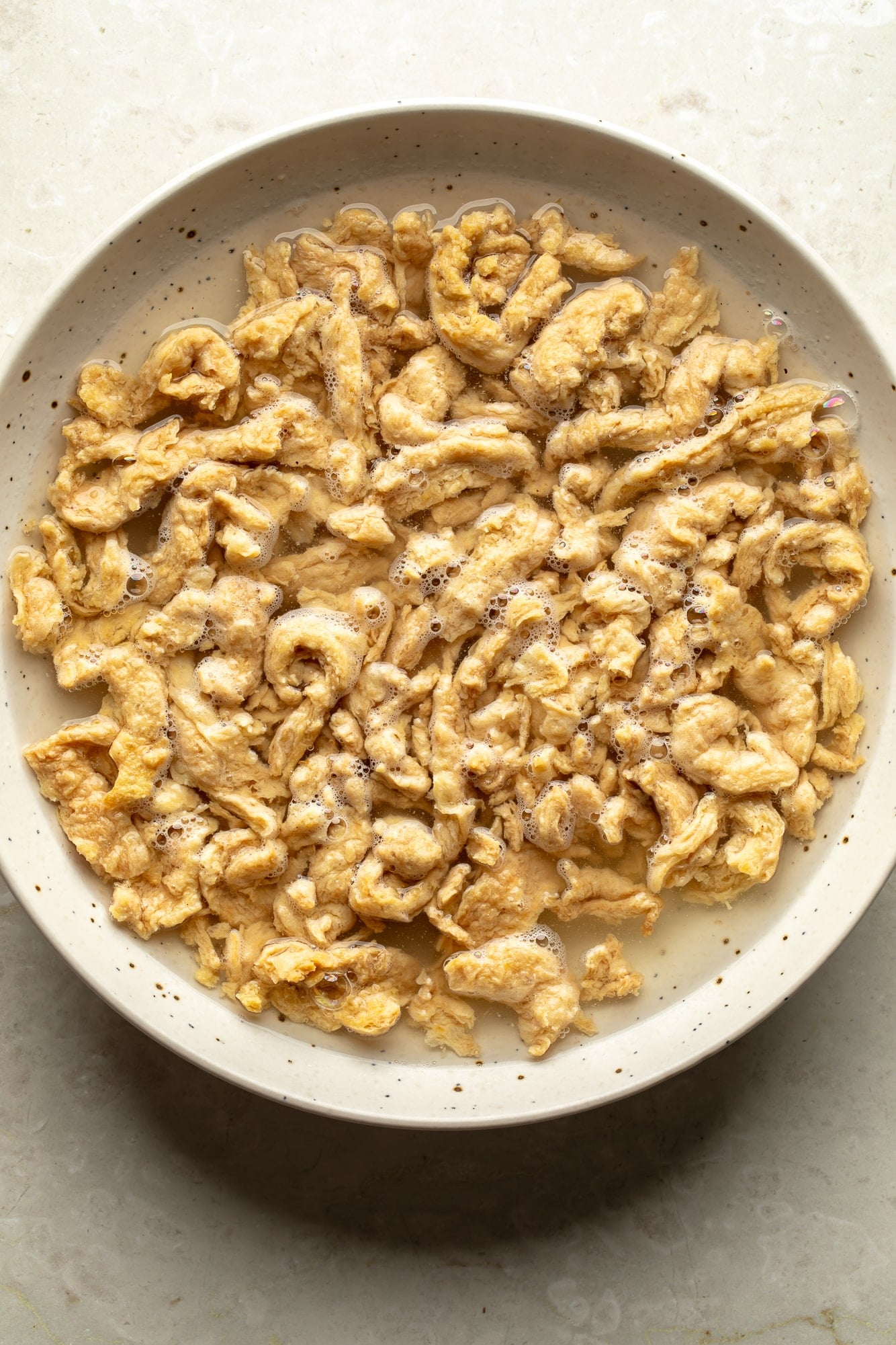 overhead view of soy curls soaking in a bowl of water for spicy peanut vegan "chicken" noodles.