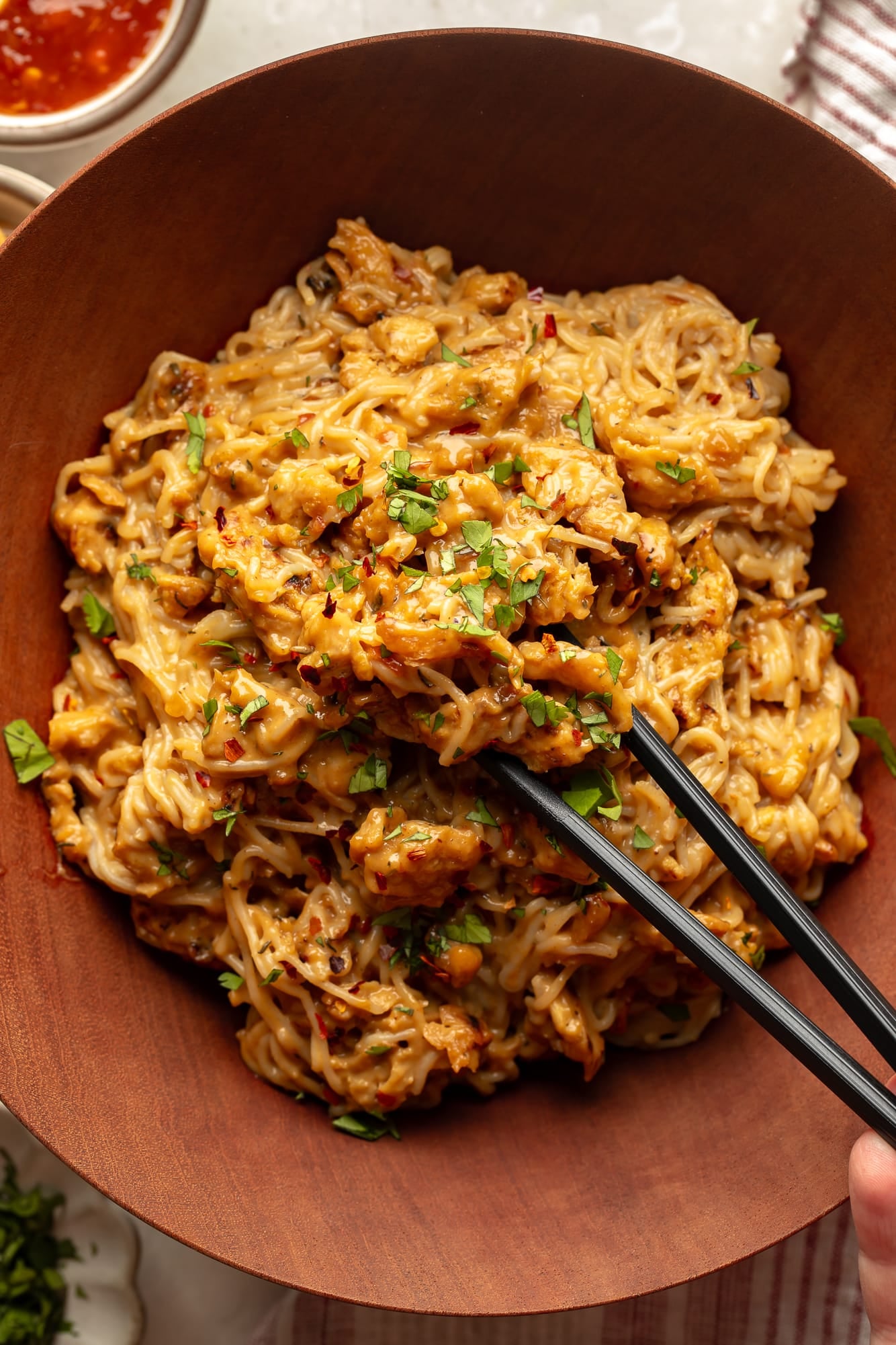 overhead view of black chopsticks picking up a bite of spicy peanut vegan "chicken" noodles from a bowl.