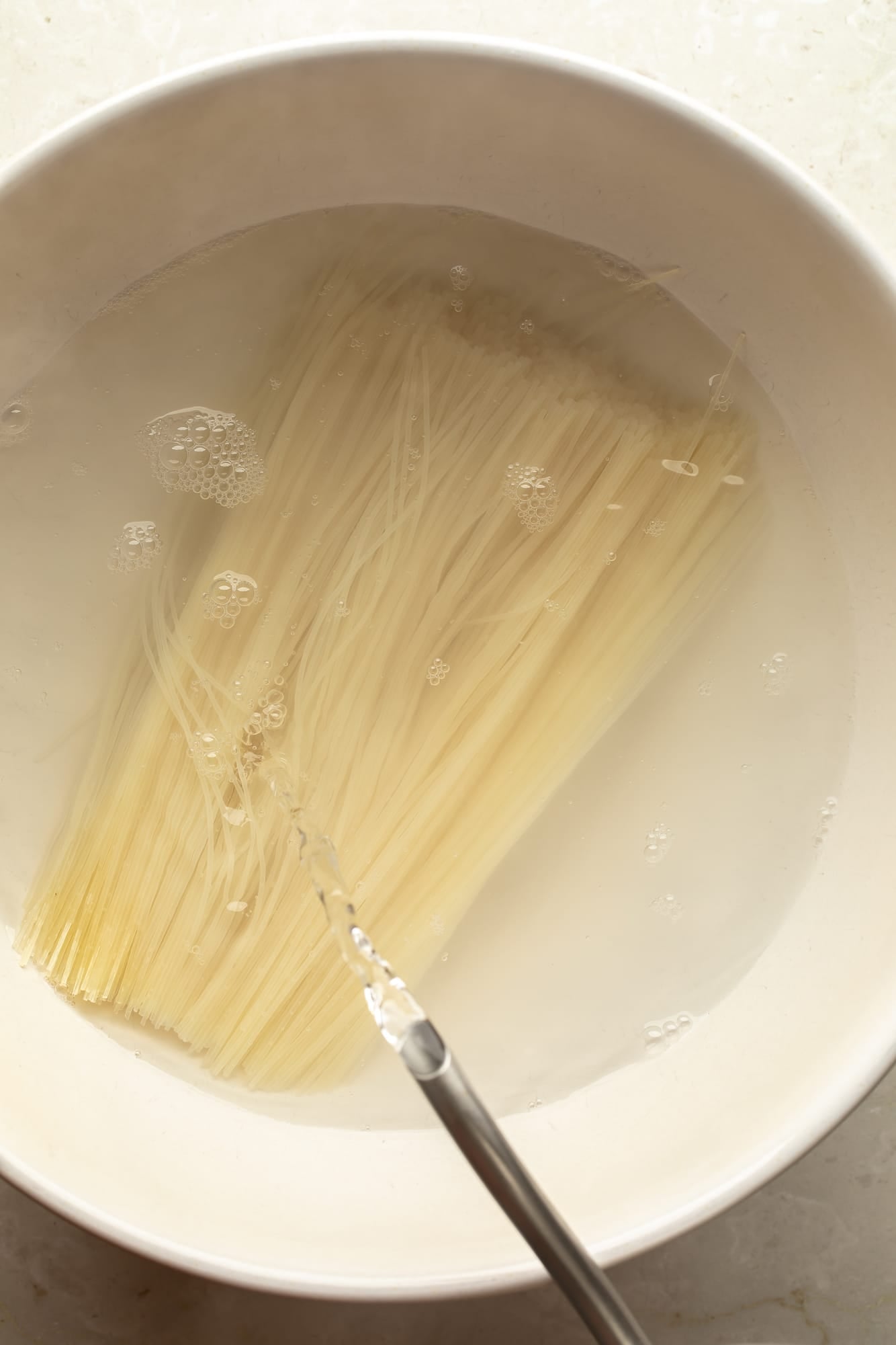 overhead view of vermicelli noodles soaking in a bowl of water for spicy peanut vegan "chicken" noodles.