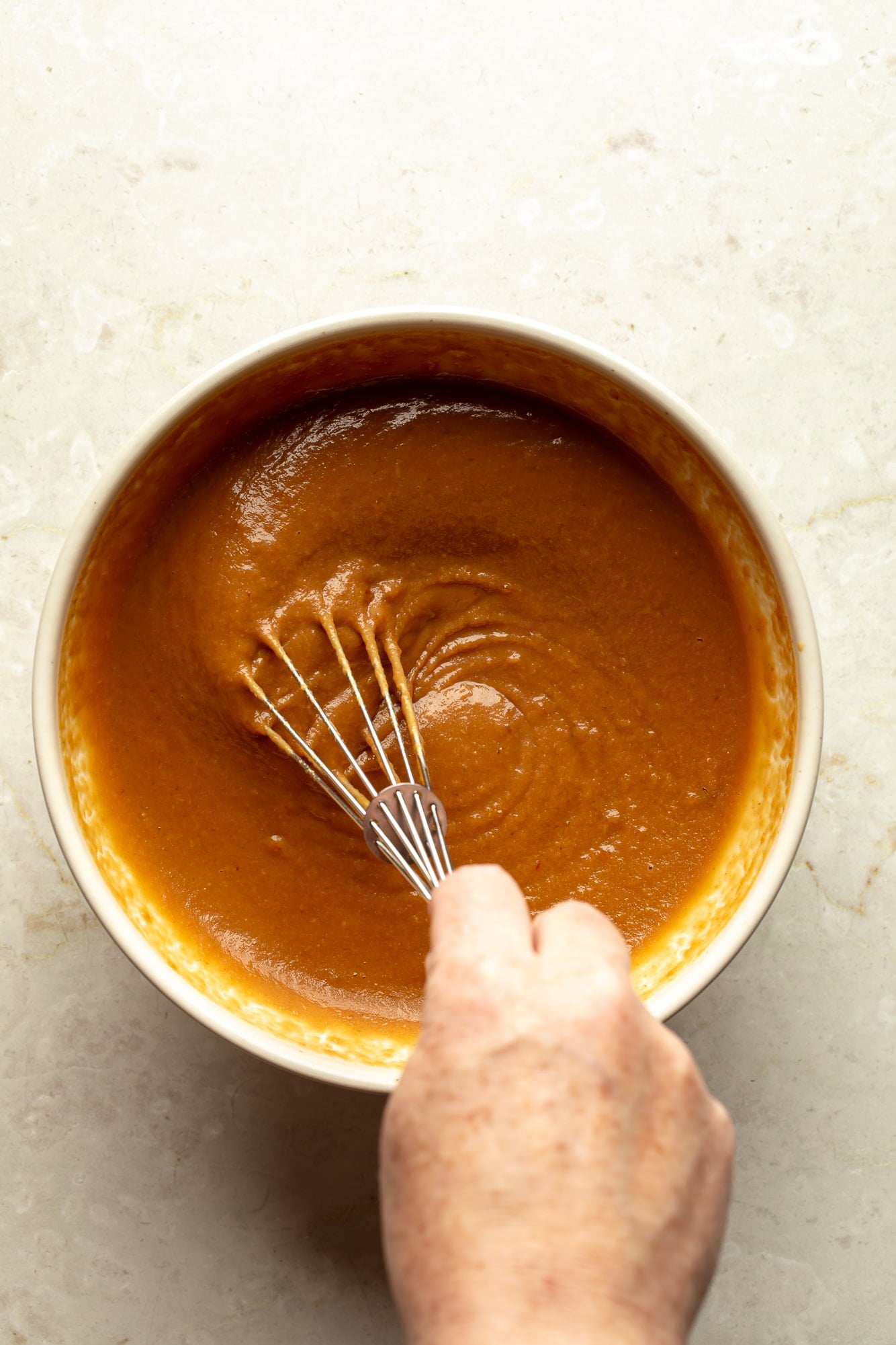 overhead view of a hand whisking a peanut sauce together in a bowl.