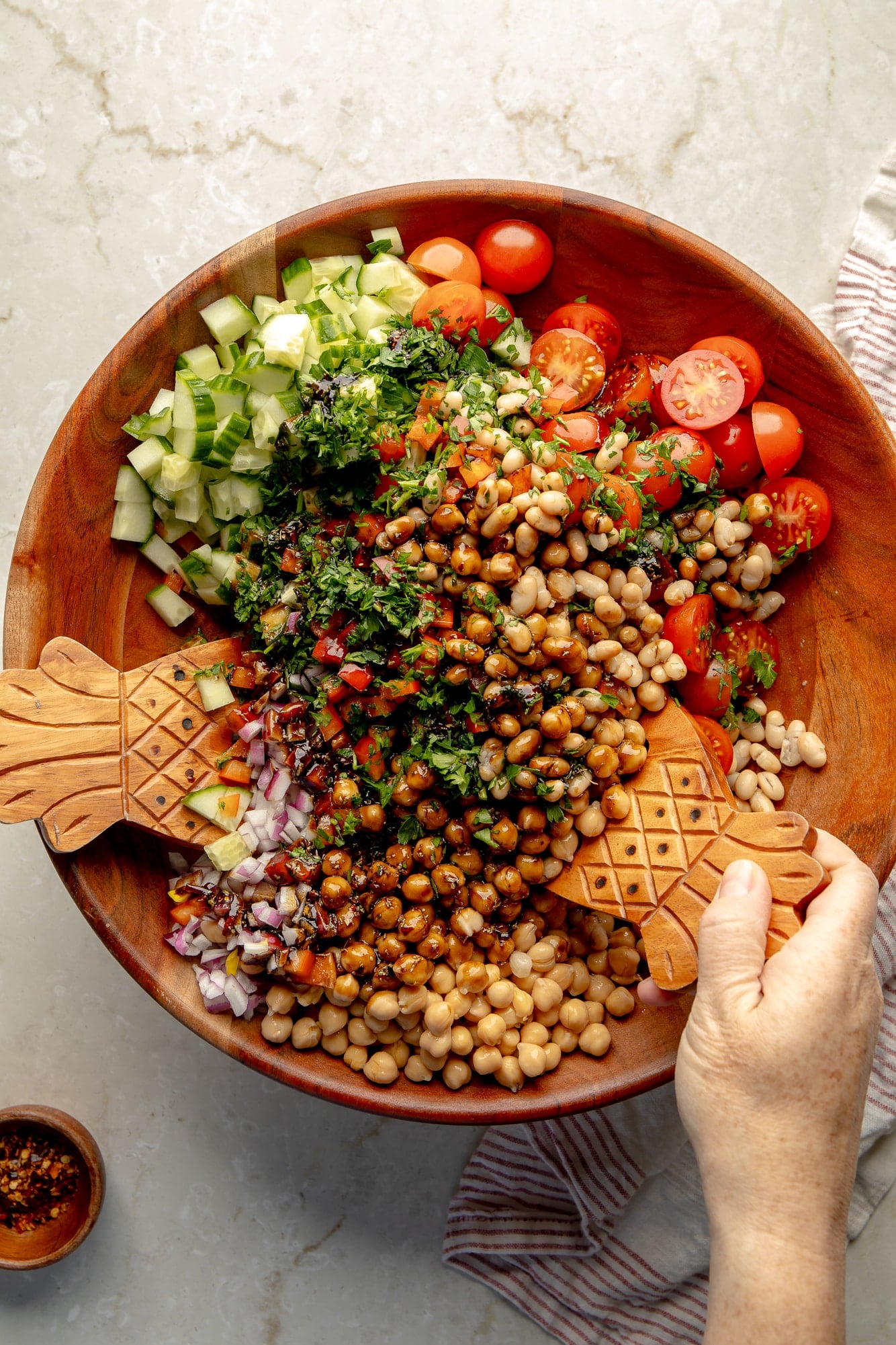 overhead view of hands using salad tongs to toss a vegan dense bean salad together in a large bamboo bowl.
