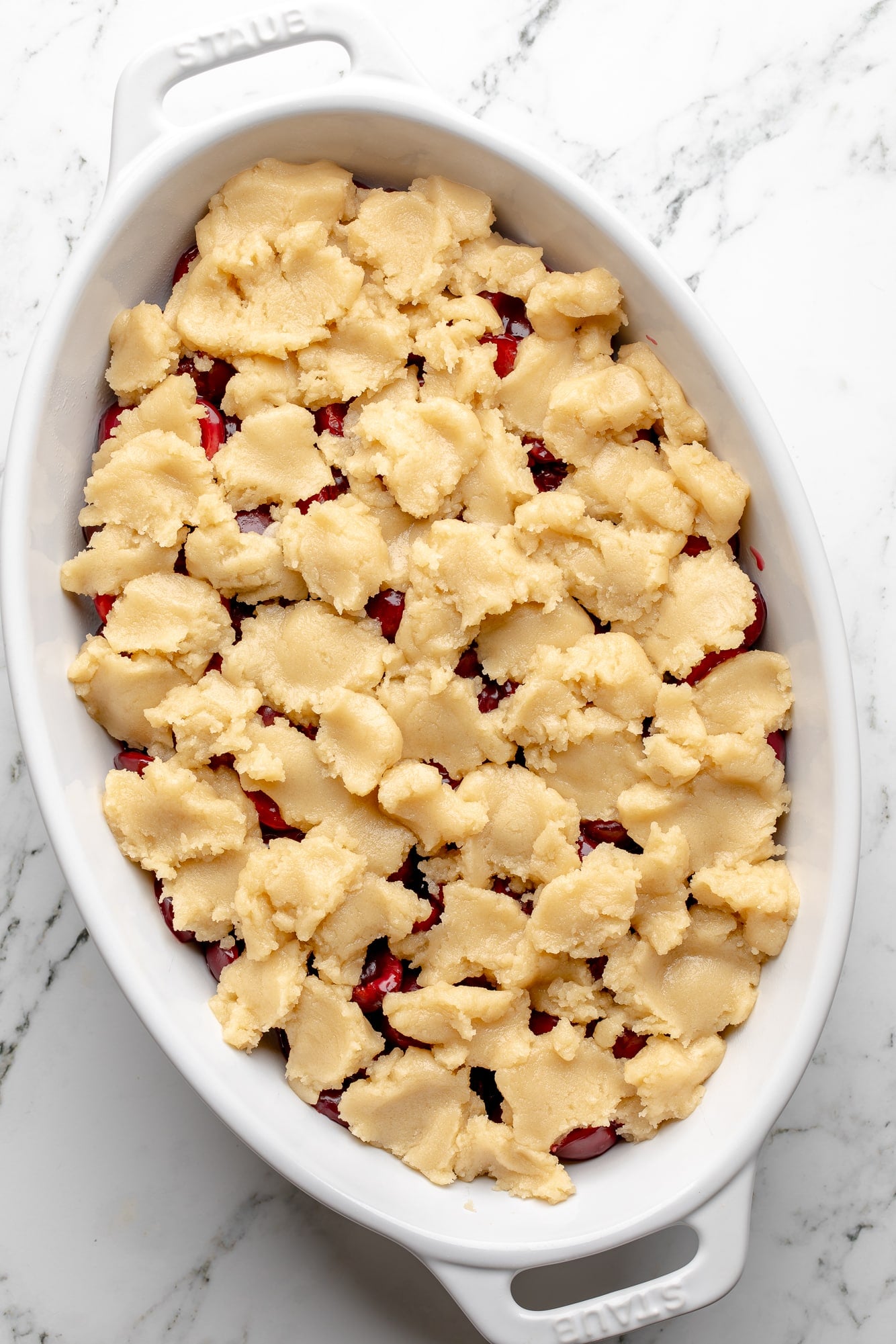 overhead view of an unbaked, dough-topped vegan cherry cobbler in a large baking dish.