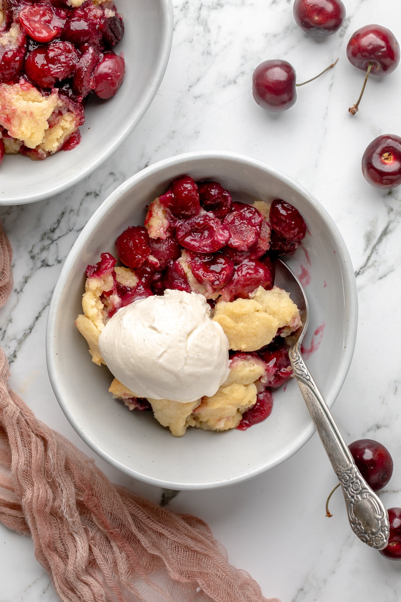 overhead view of a serving of vegan cherry cobbler topped with a scoop of vanilla ice cream in a bowl.