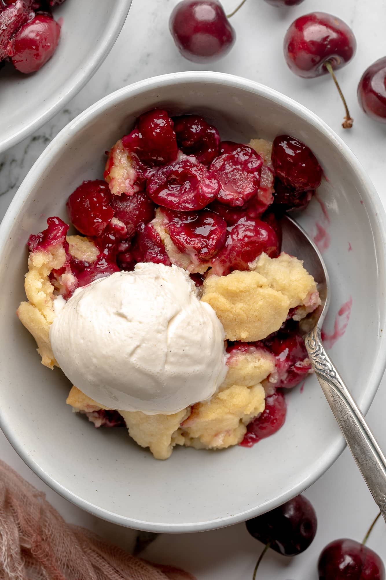 overhead view of a serving of vegan cherry cobbler topped with a scoop of vanilla ice cream in a bowl.