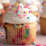 side view of a vegan funfetti cupcake topped with vanilla icing and colorful sprinkles.
