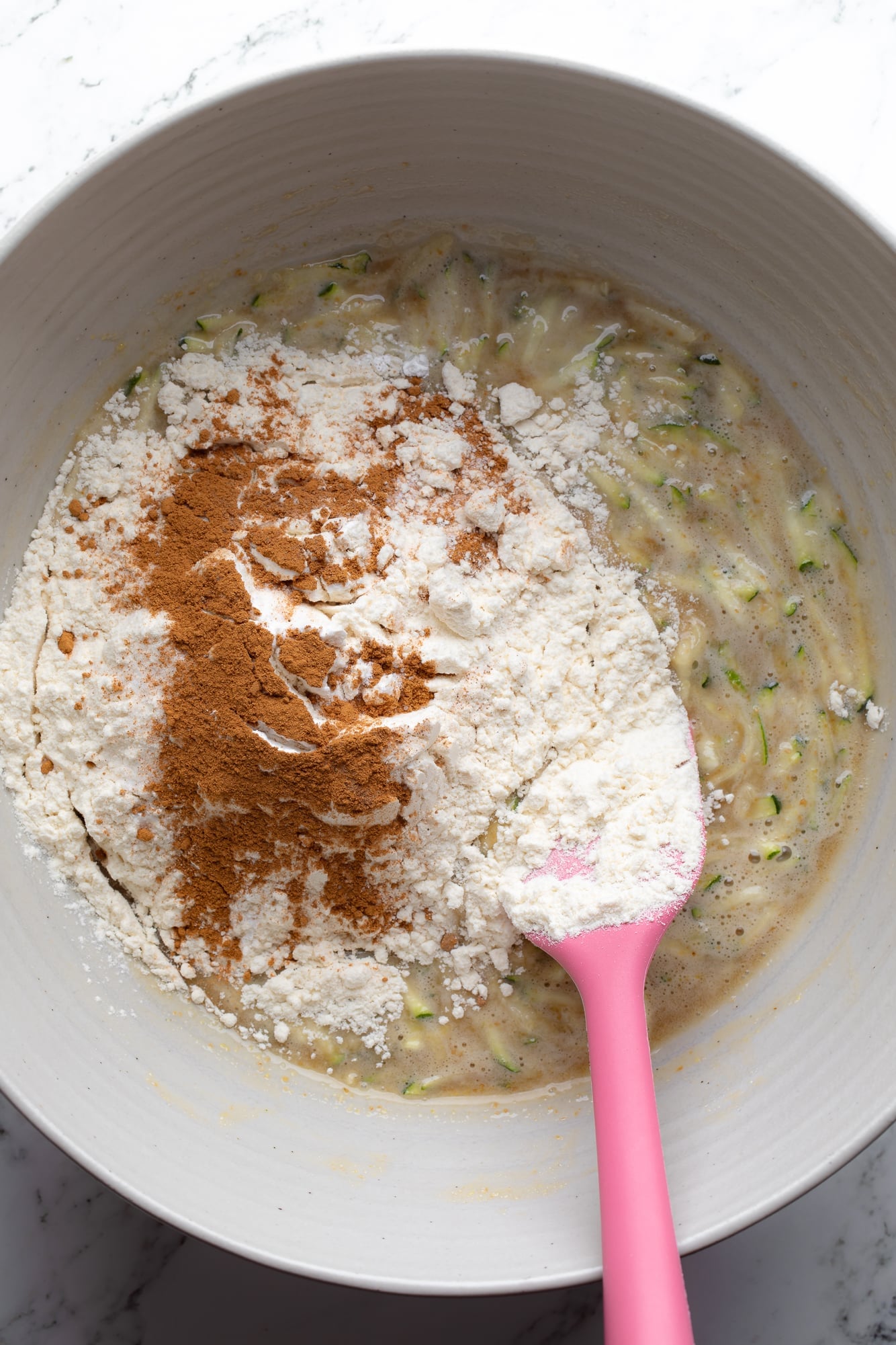 overhead view of a pink spatula stirring dry ingredients into vegan zucchini muffin batter.