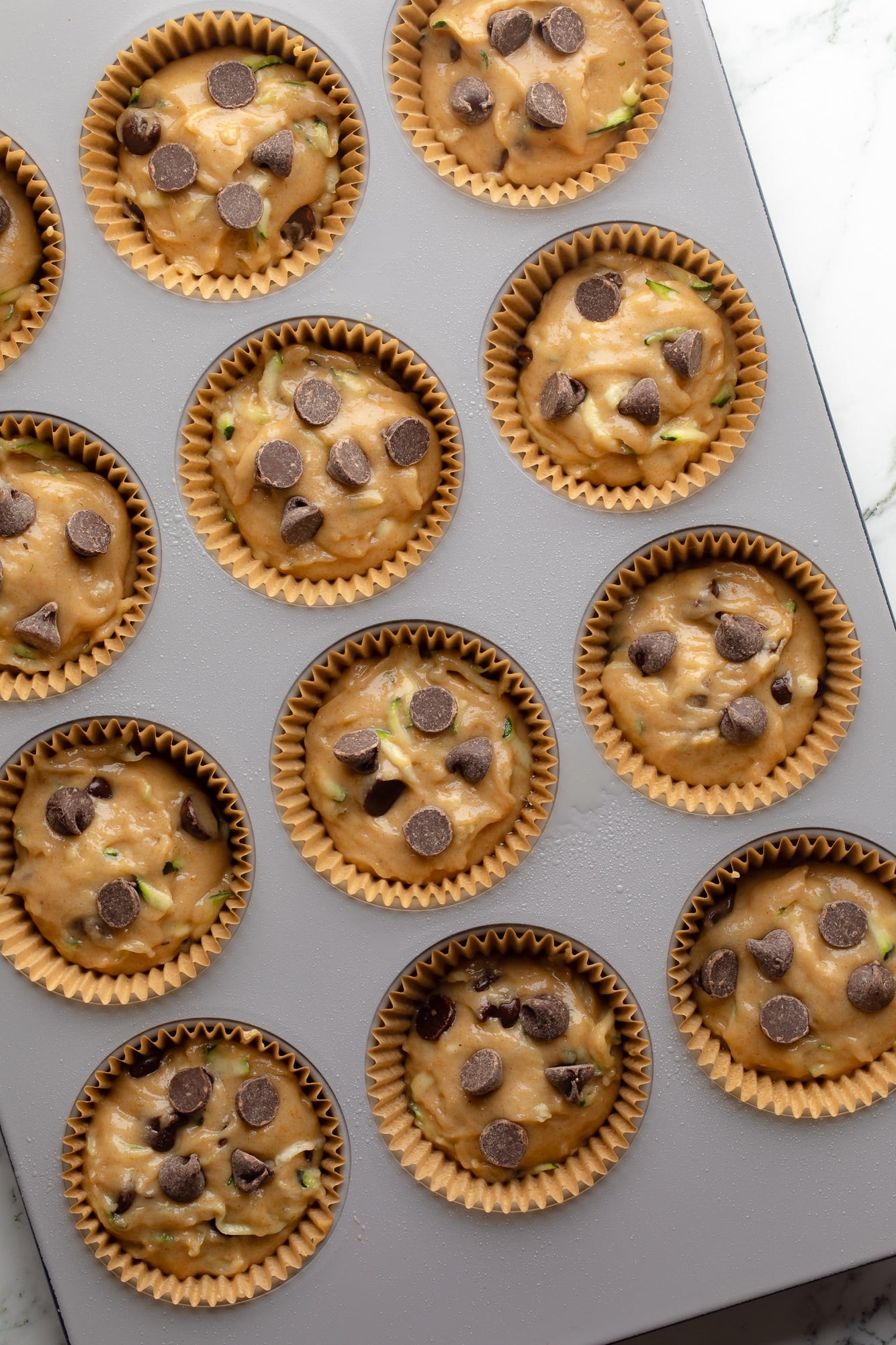 overhead view of unbaked vegan zucchini muffins in a muffin tin .