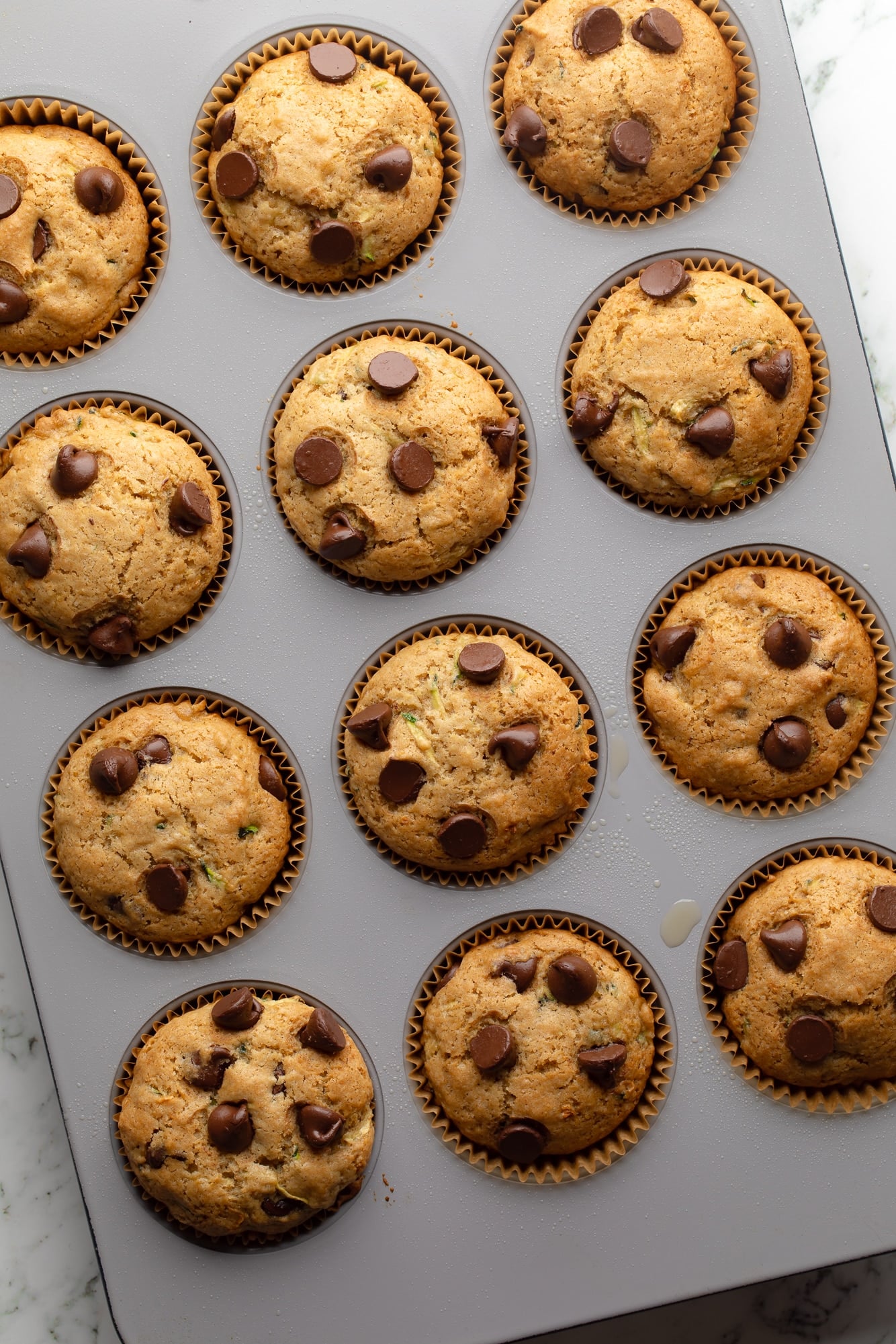 overhead view of baked vegan zucchini muffins in a muffin tin .