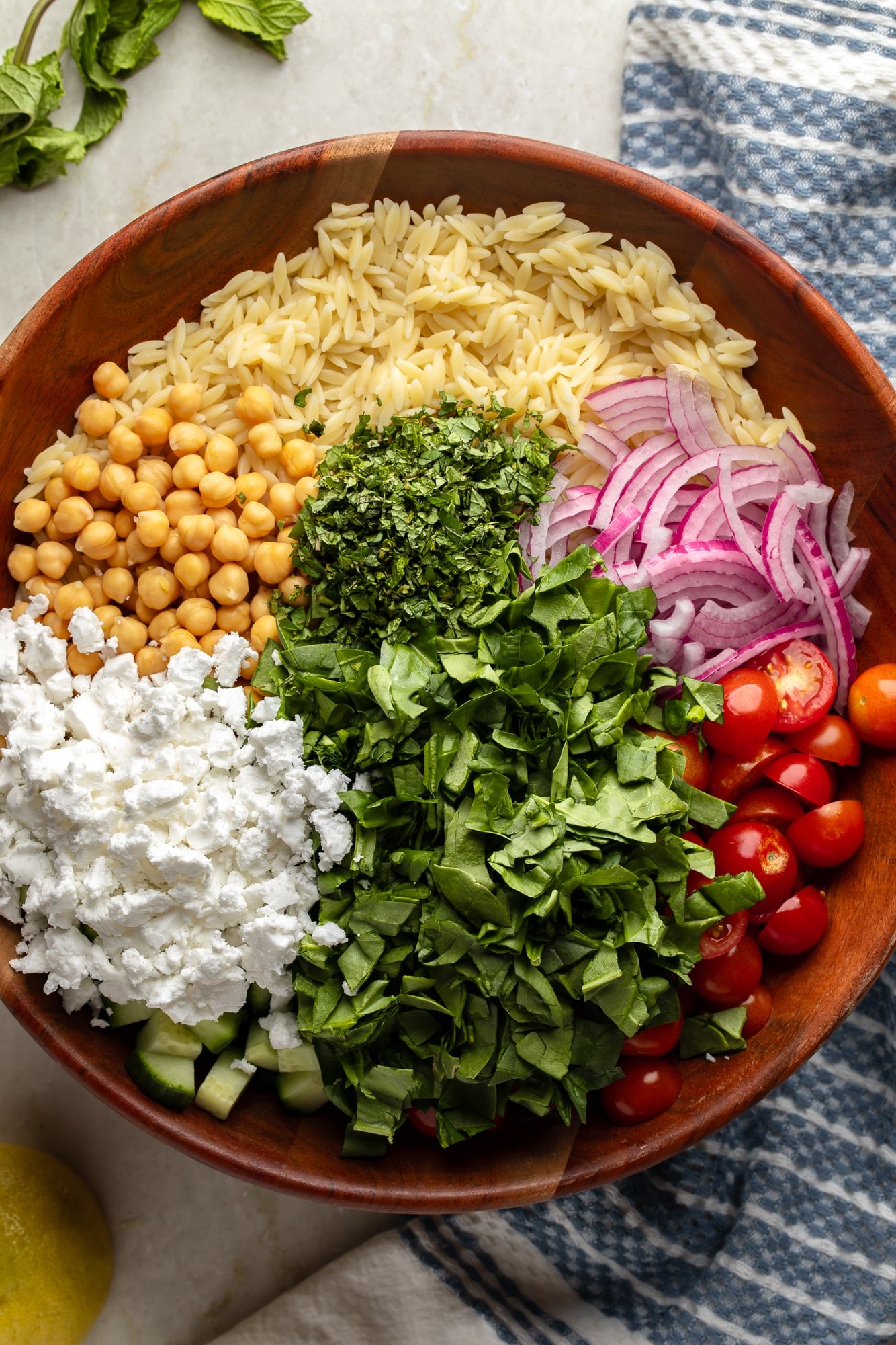 overhead view of the ingredients for a lemon orzo pasta salad in a large bamboo bowl.