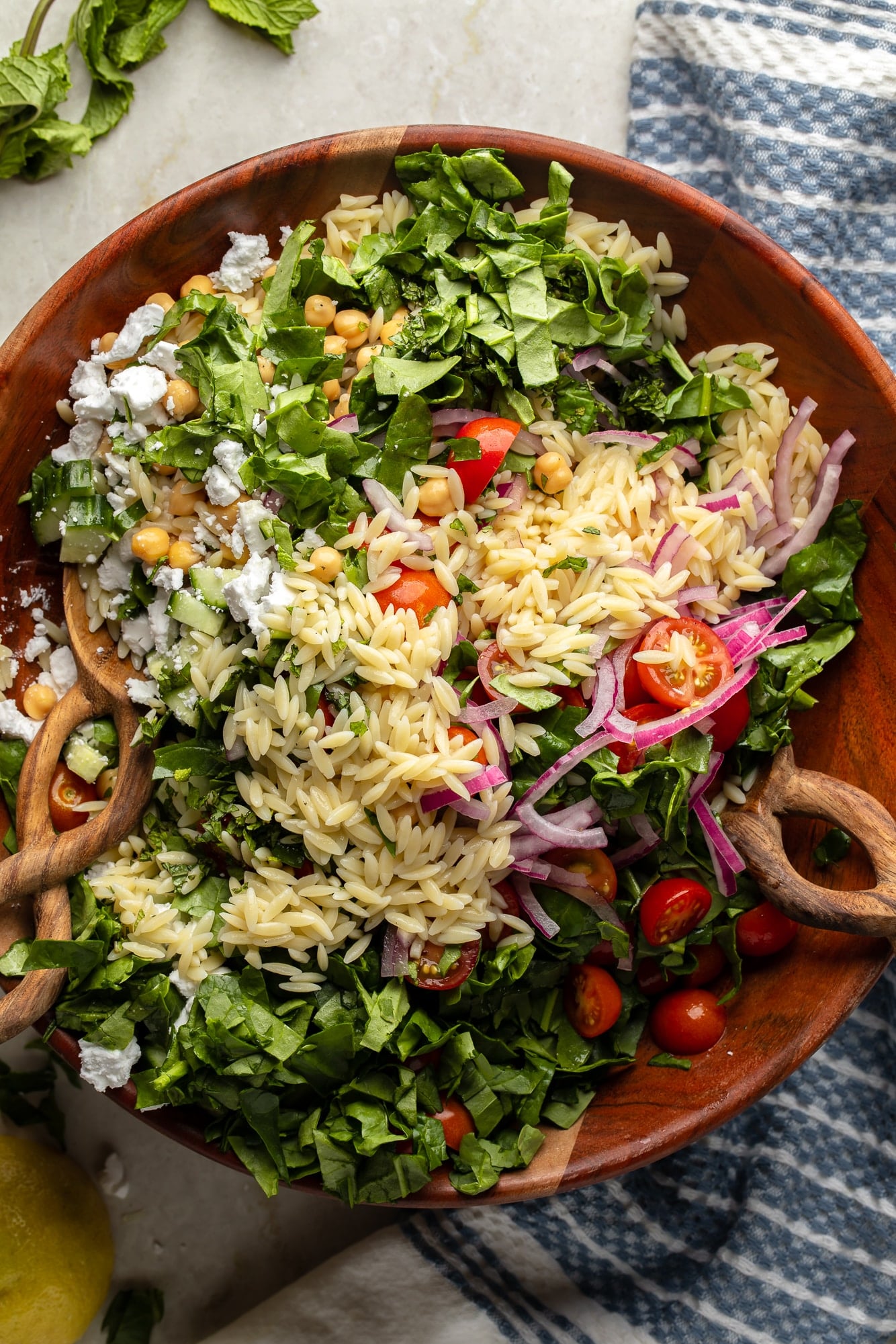 overhead view of a lemon orzo pasta salad and salad tongs in a large bamboo bowl.