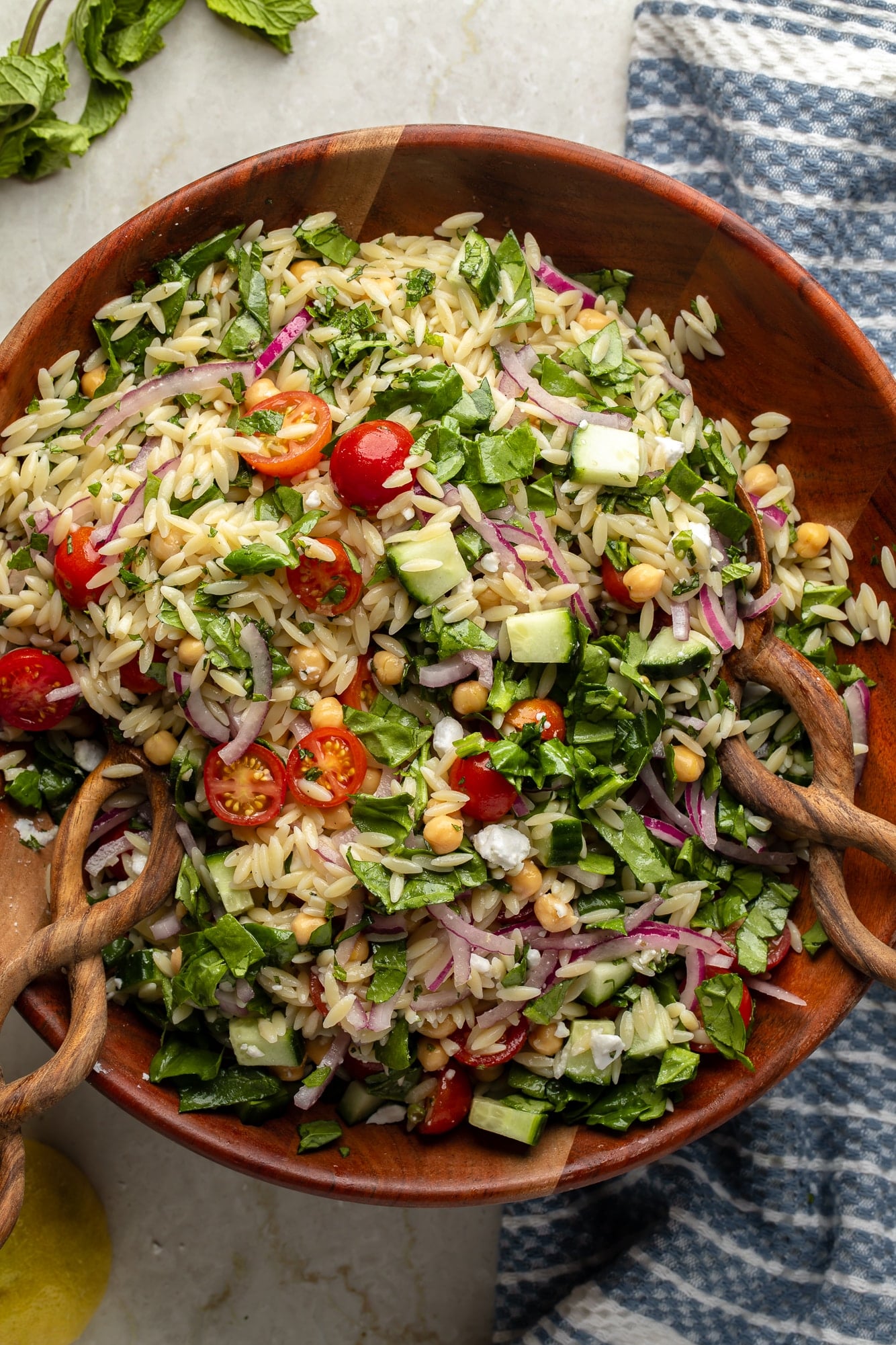 overhead view of a lemon orzo pasta salad and salad tongs in a large bamboo bowl.