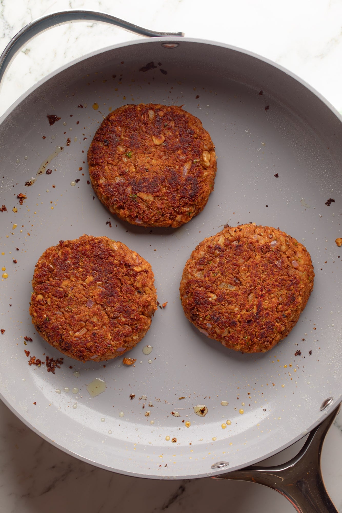 overhead view of 3 lentil burgers frying in a skillet.